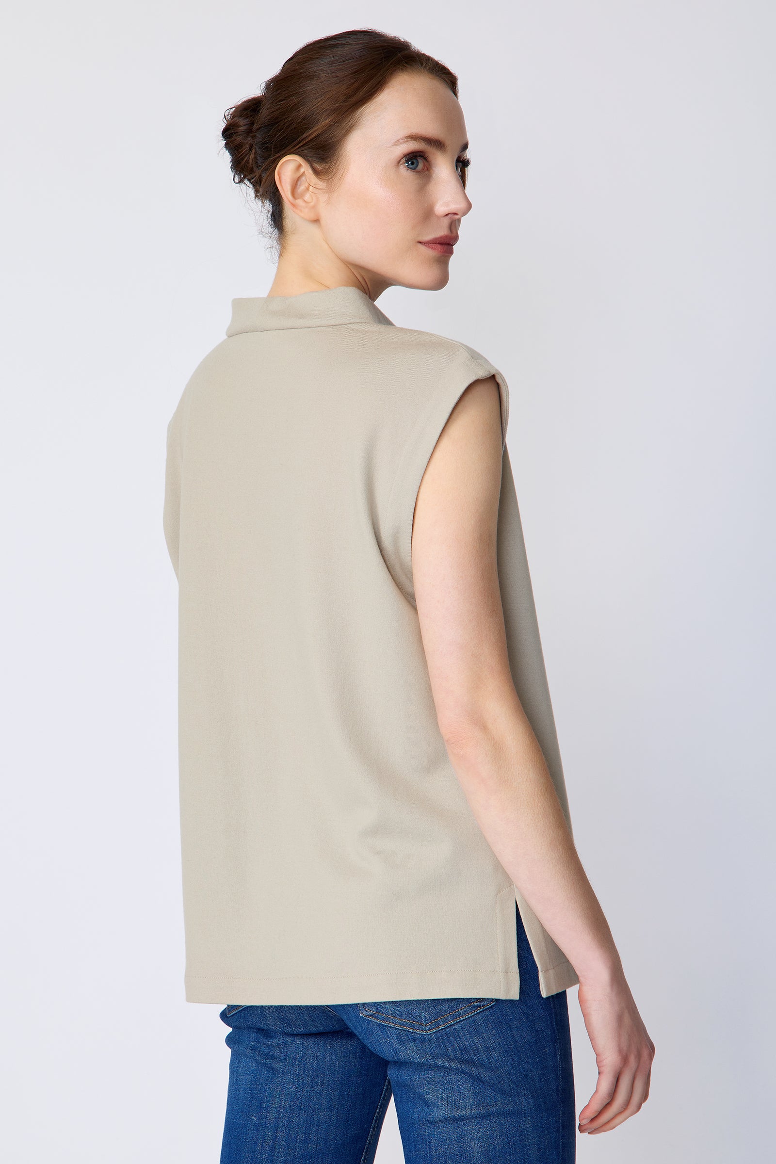 Woman wearing Kal Rieman Arla Drape Top in Mink Felted Jersey and blue jeans on a white background, arms on the side, back view