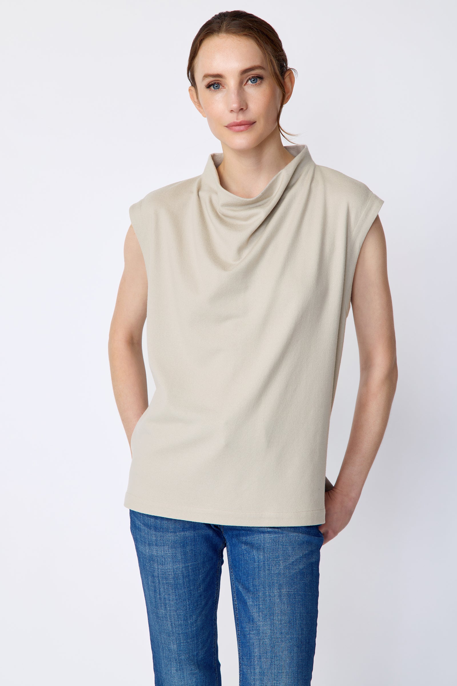 Woman wearing Kal Rieman Arla Drape Top in Mink Felted Jersey and blue jeans on a white background, hands in back pant pockets
