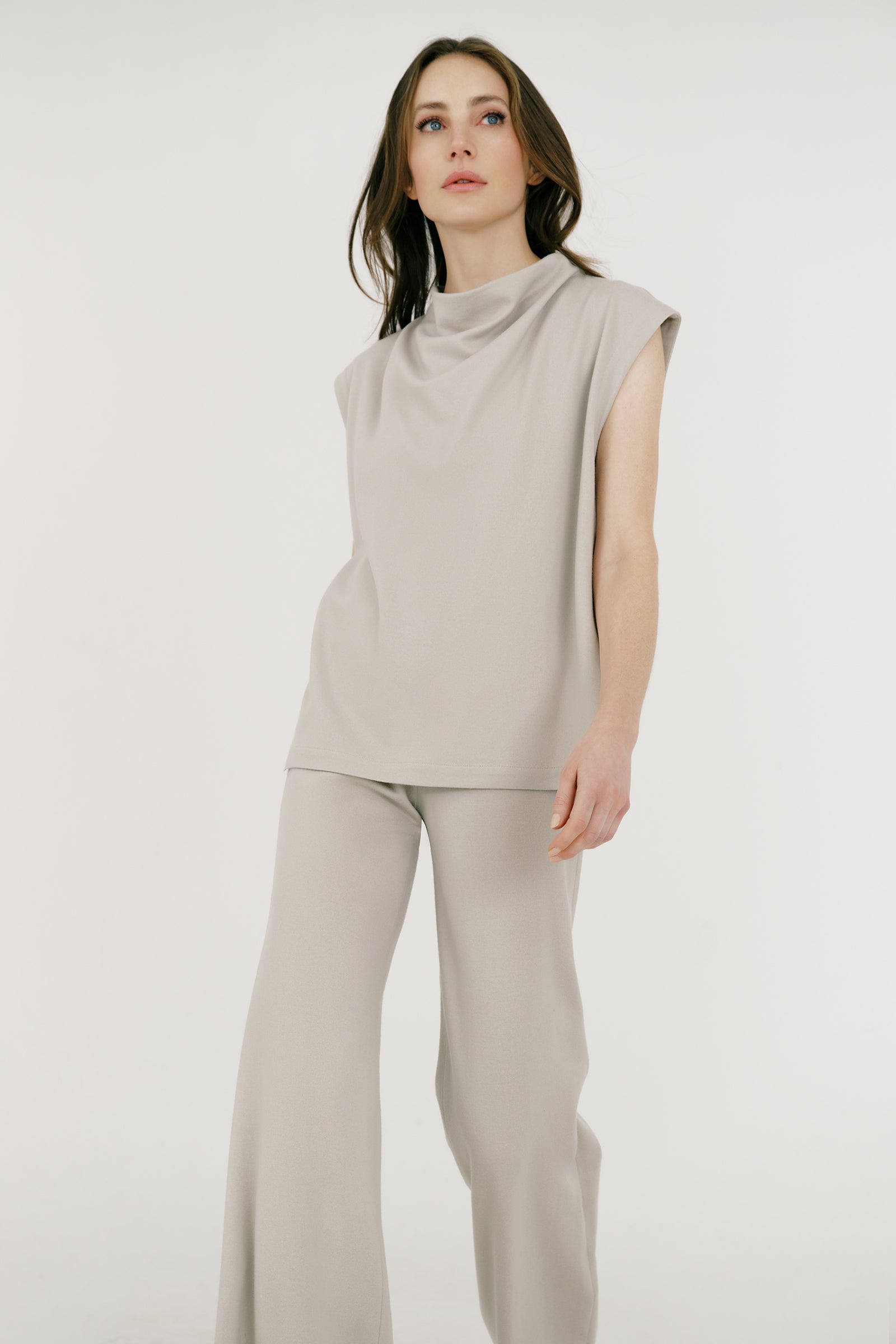 Woman wearing Kal Rieman Arla Drape Top in Mink Felted Jersey and blue jeans on a white background, hands in back pant pockets