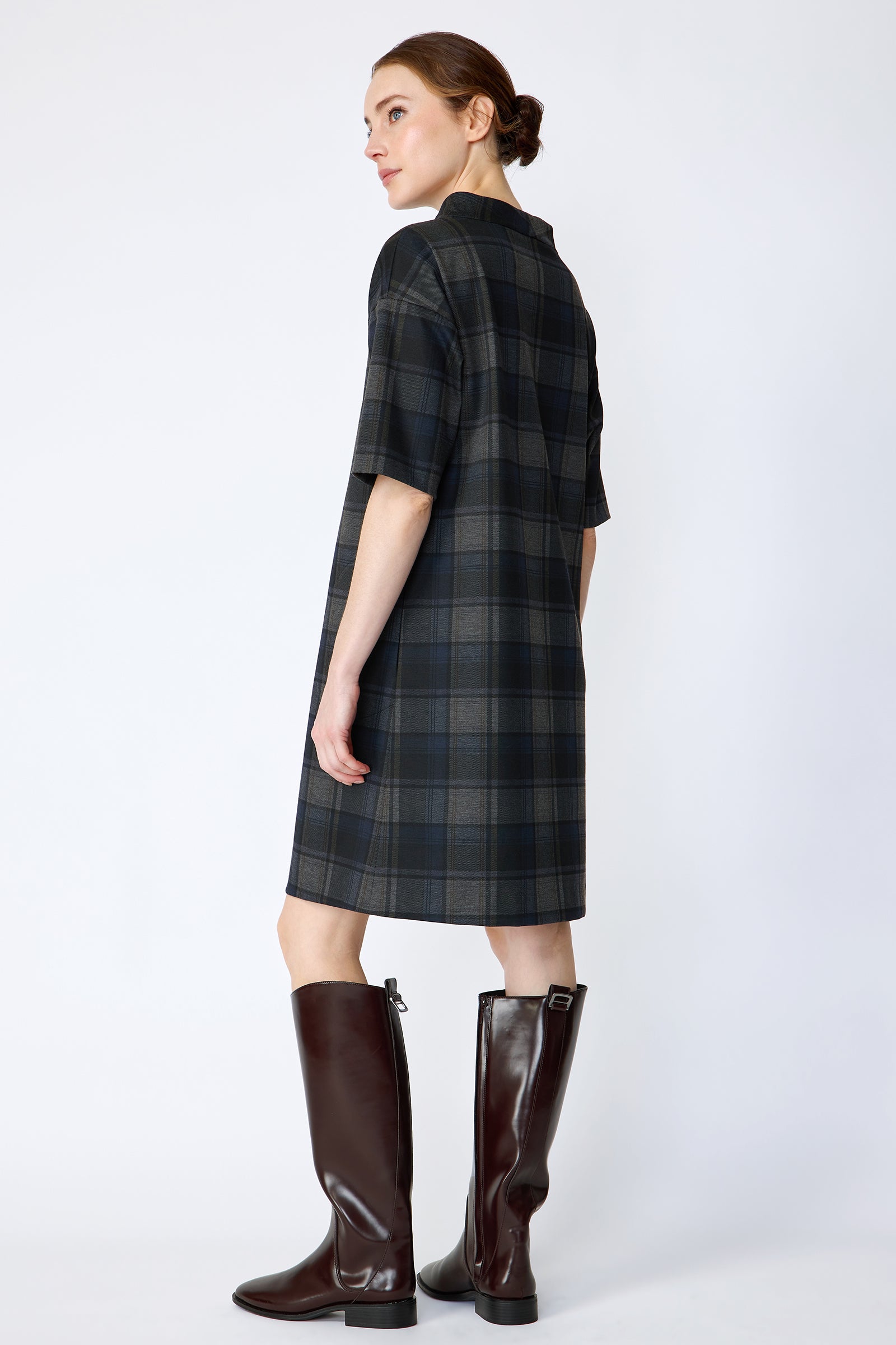Woman wearing Kal Rieman Avery Shift Dress in Novelty Plaid with knee-high boots on a white background arms on the side back view