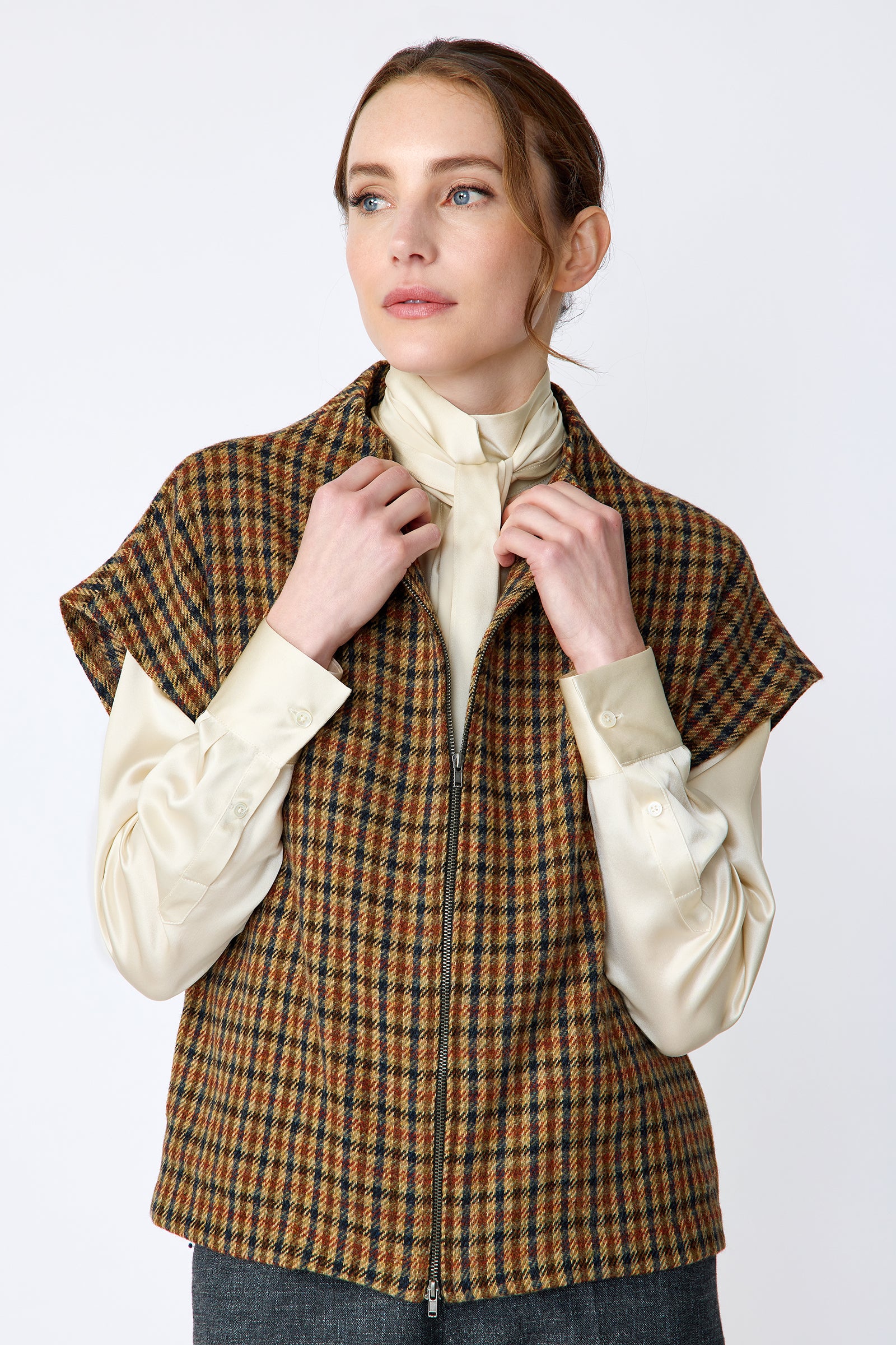 Woman wearing Kal Rieman Bruna Zip Vest in Heritage Check over a Kal Rieman Silk Regency Blouse in Oyster with a white background, hands holding collar