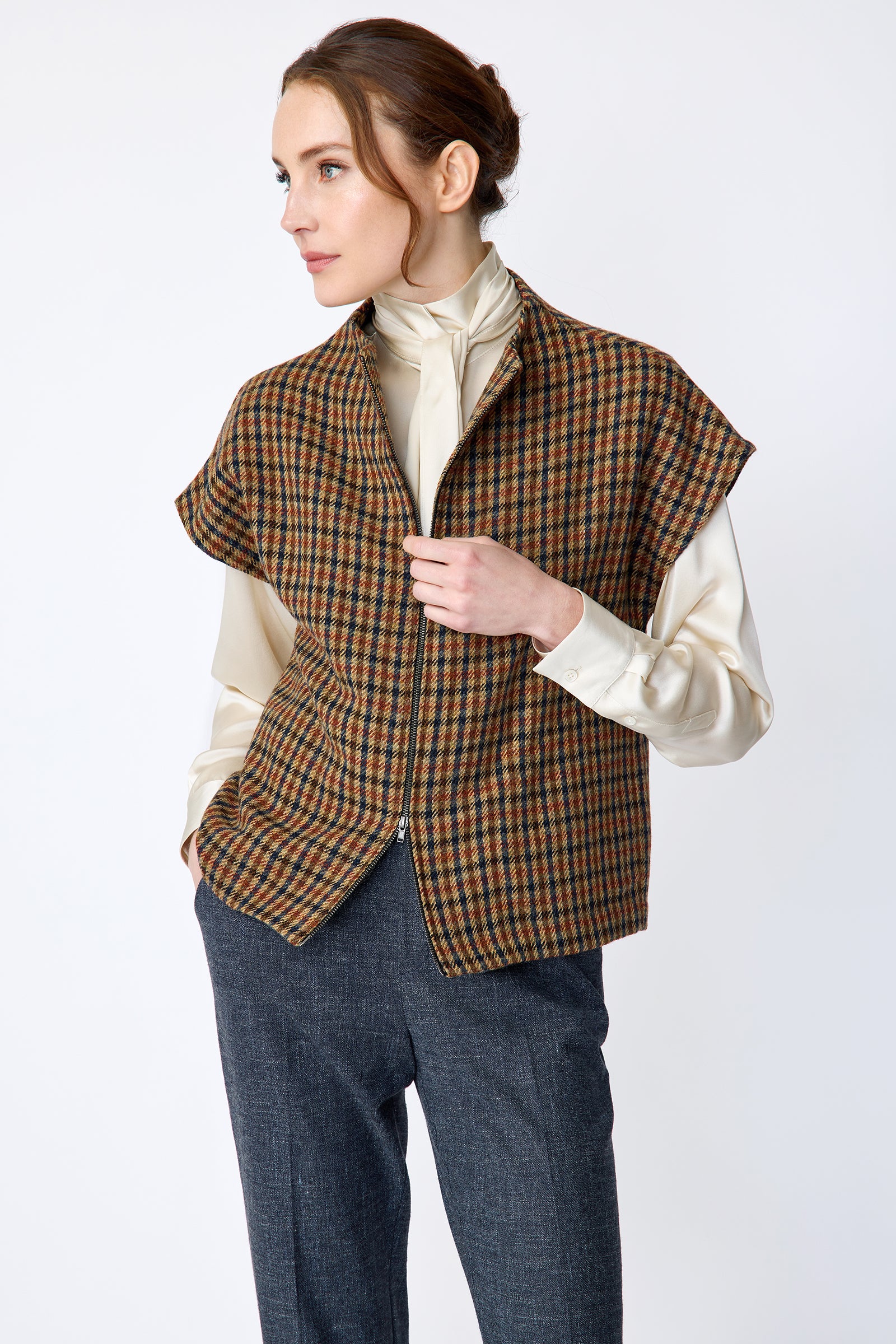 Woman wearing Kal Rieman Bruna Zip Vest in Heritage Check over a Kal Rieman Silk Regency Blouse in Oyster with a white background, arm in pocket and hand holding zipper