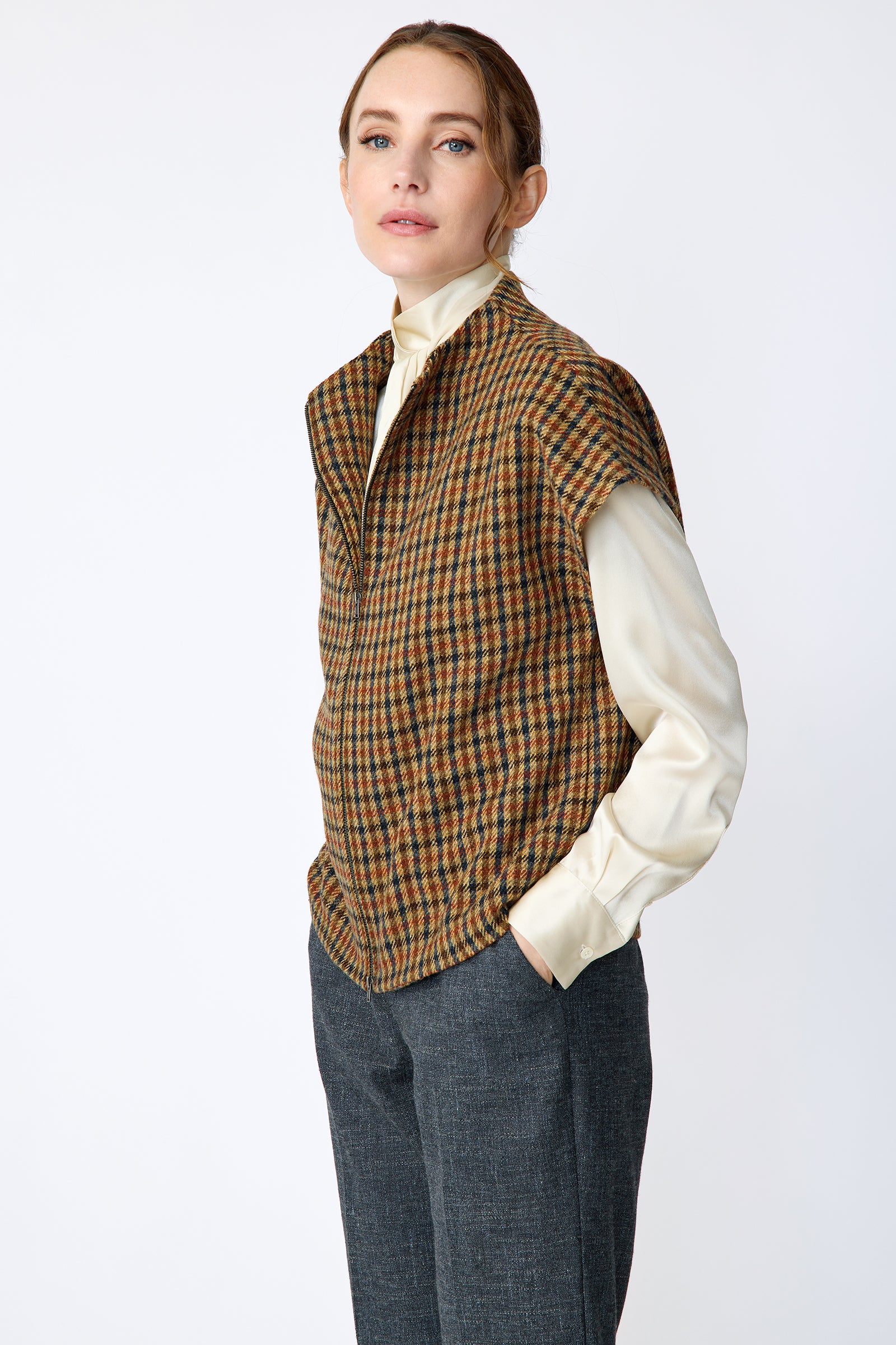 Woman wearing Kal Rieman Bruna Zip Vest in Heritage Check over a Kal Rieman Silk Regency Blouse in Oyster with a white background, hands in pocket side view