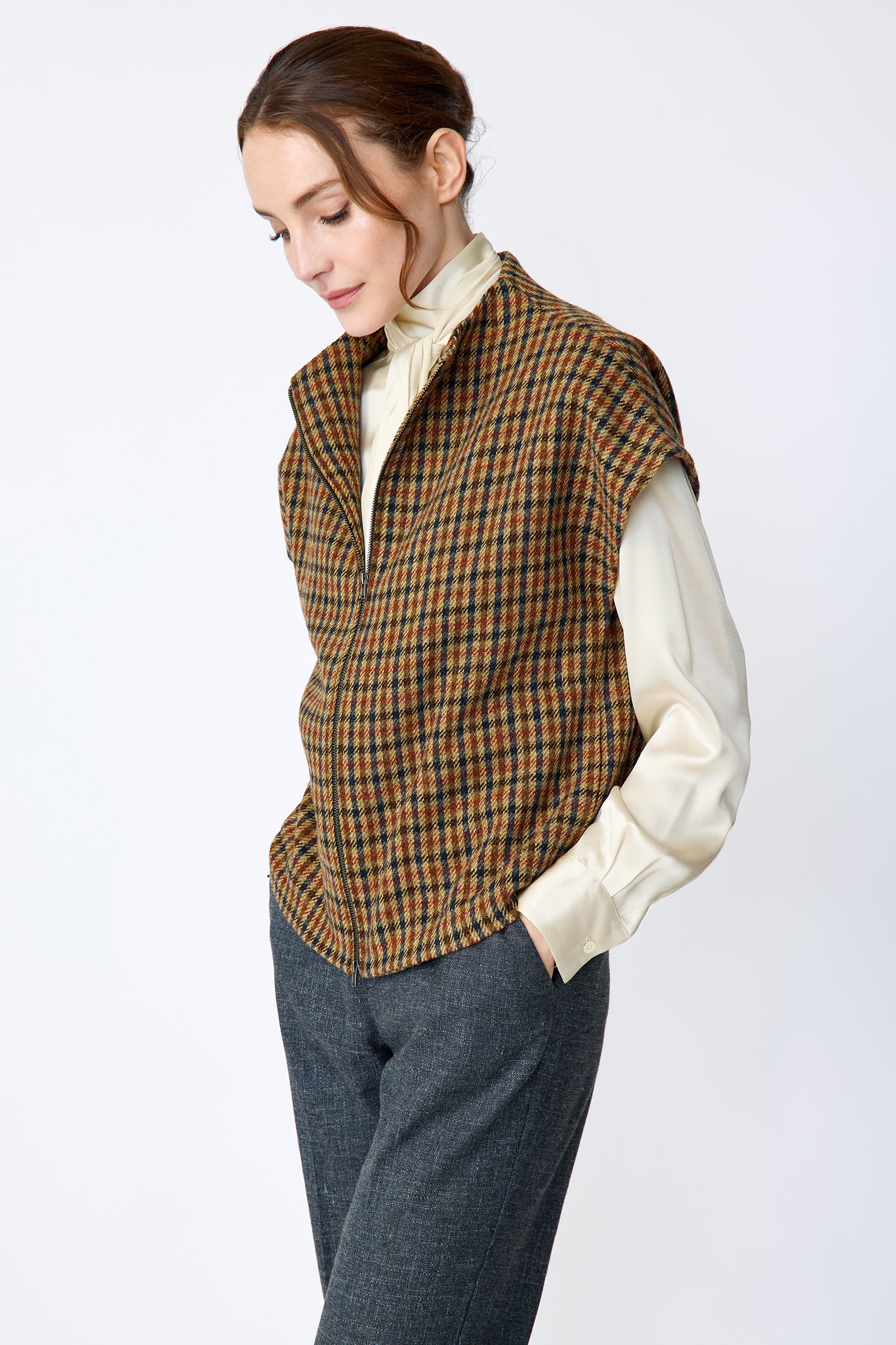 Woman wearing Kal Rieman Bruna Zip Vest in Heritage Check over a Kal Rieman Silk Regency Blouse in Oyster with a white background, arms in pocket side view looking down