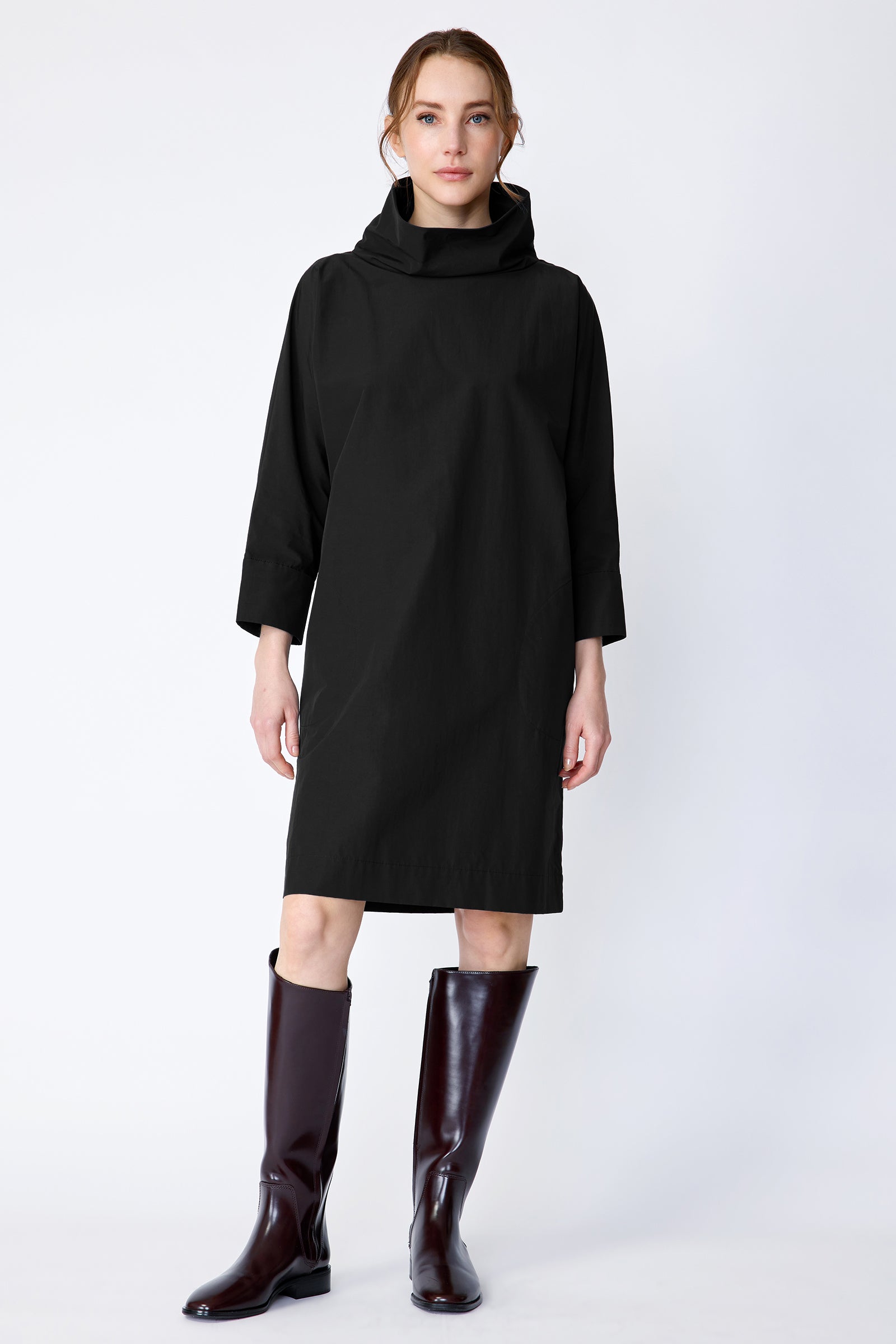 Woman wearing Kal Rieman Carla black dress and brown boots on a white background