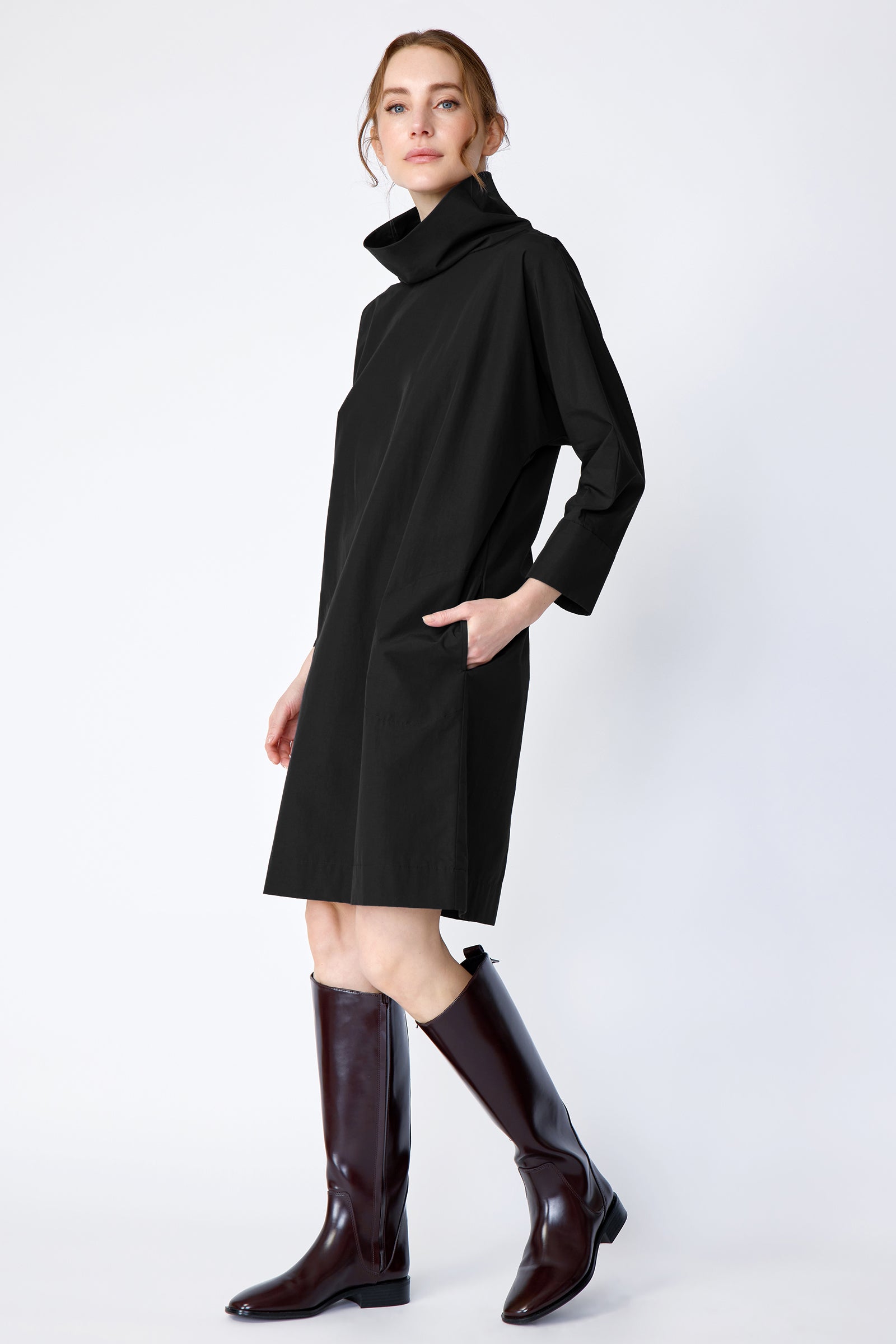 Woman wearing Kal Rieman Carla black dress and brown boots on a white background side view walking