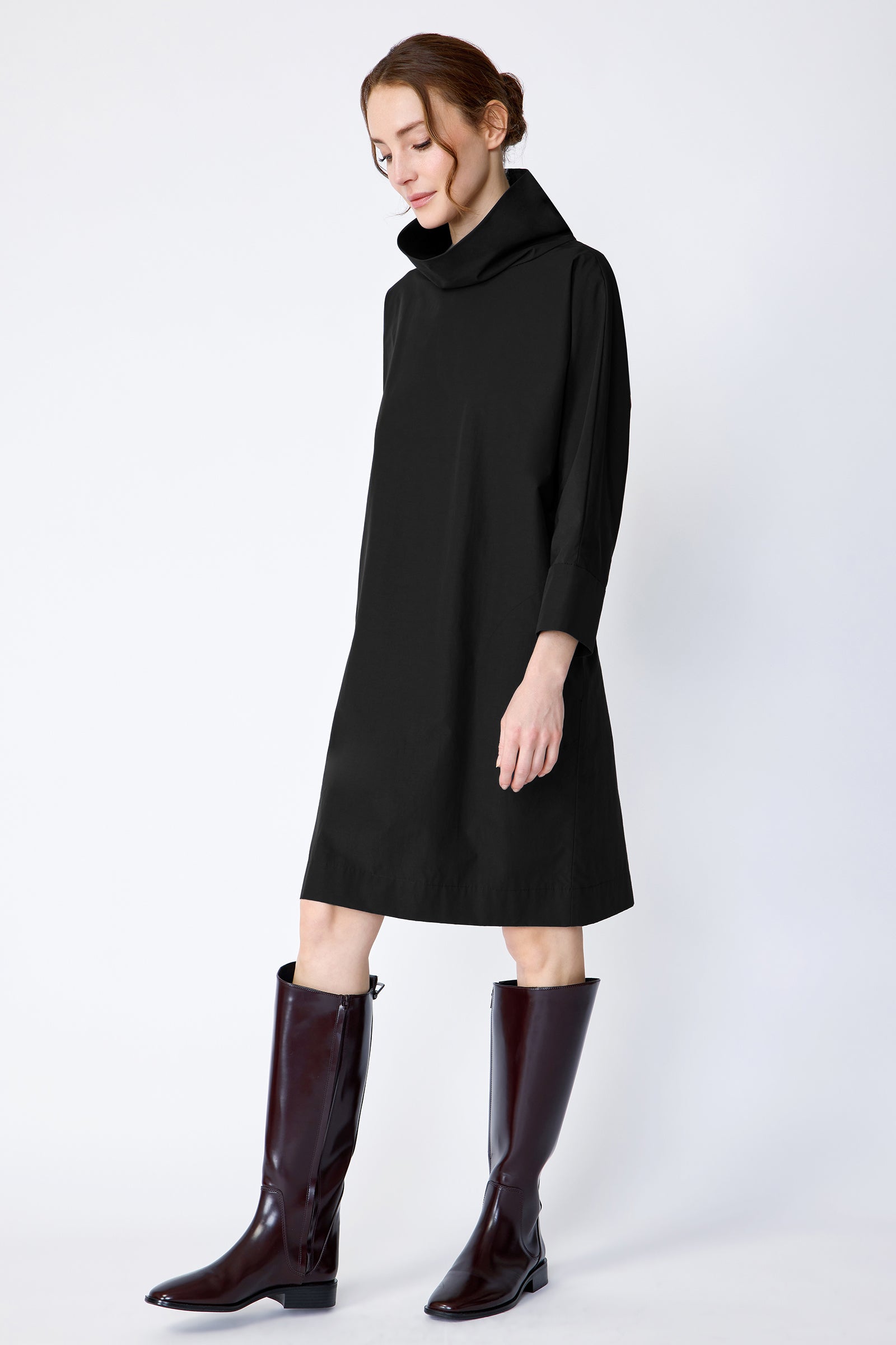 Woman wearing Kal Rieman Carla black dress and brown boots on a white background looking down