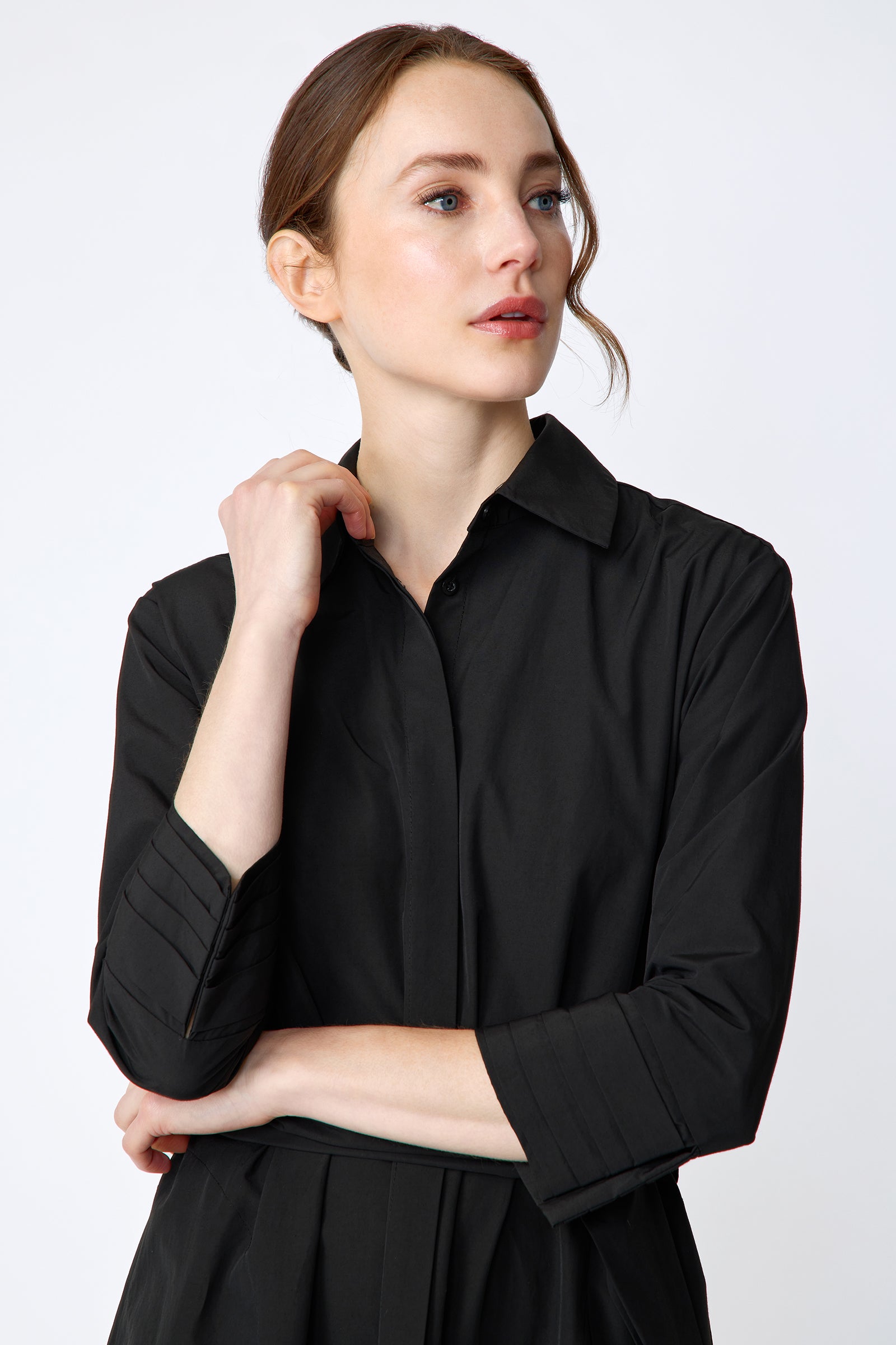 Woman wearing Kal Rieman Carolina Dress in Black Italian Broadcloth with burgundy shoes, against a white background, hand holding collar, arm crossed in front, close view