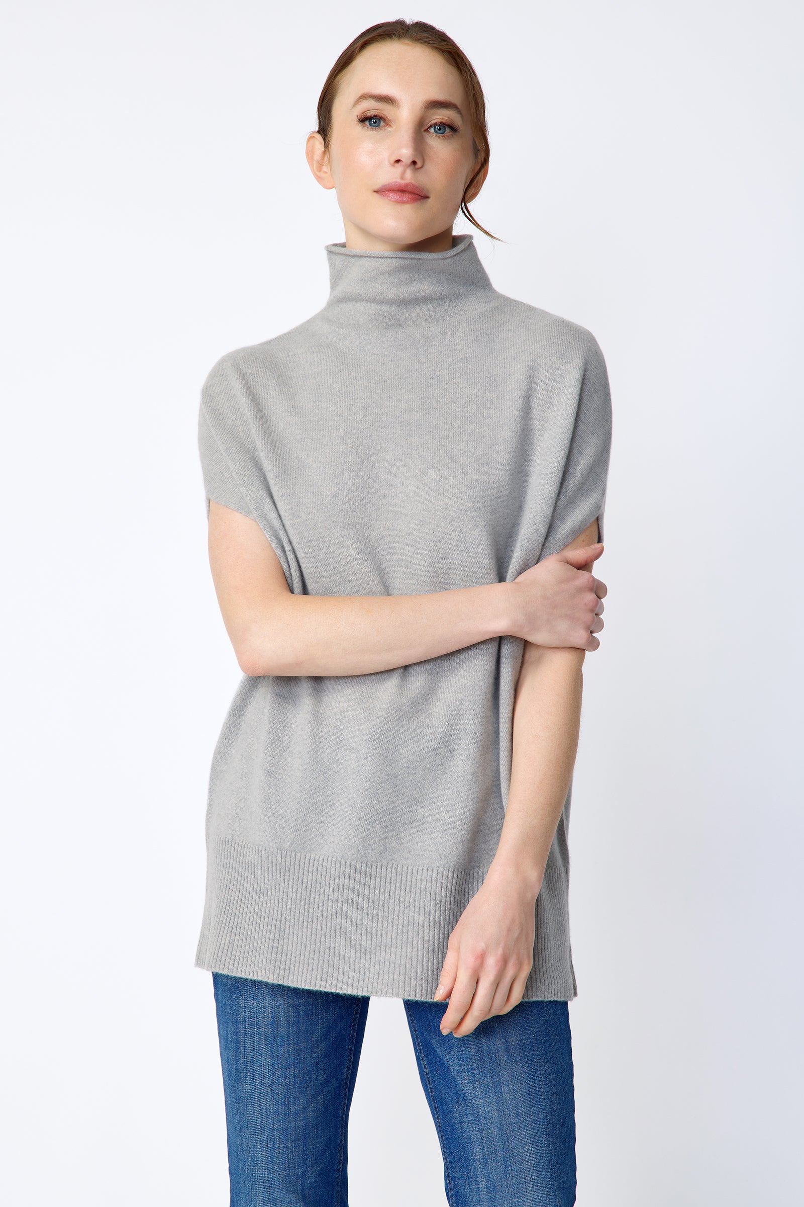 Woman wearing Kal Rieman Cashmere Funnelneck in Heather gray, blue jeans, and brown shoes on a white background arm crossed in front close view