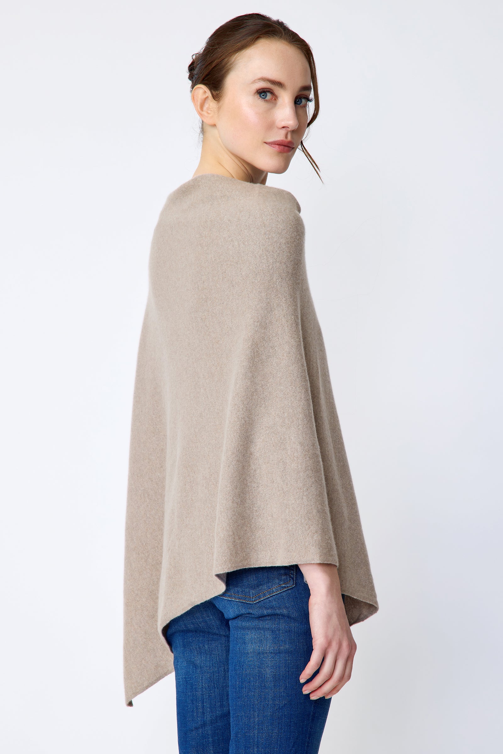 Woman wearing Kal Rieman Poncho in Drift over a blue top and blue jeans on a white background back view