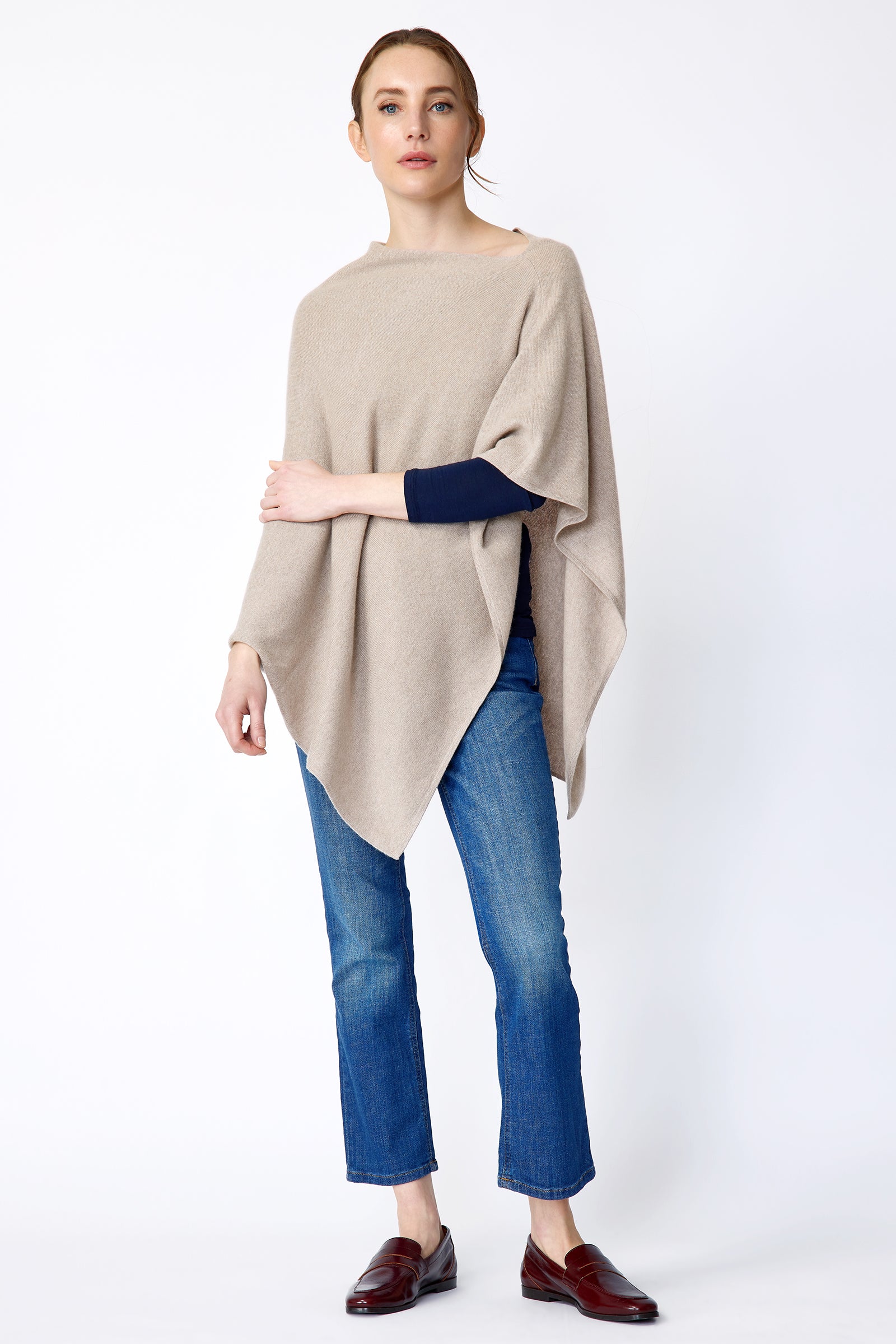 Woman wearing Kal Rieman Poncho in Drift over a blue top and blue jeans on a white background arm crossed in front