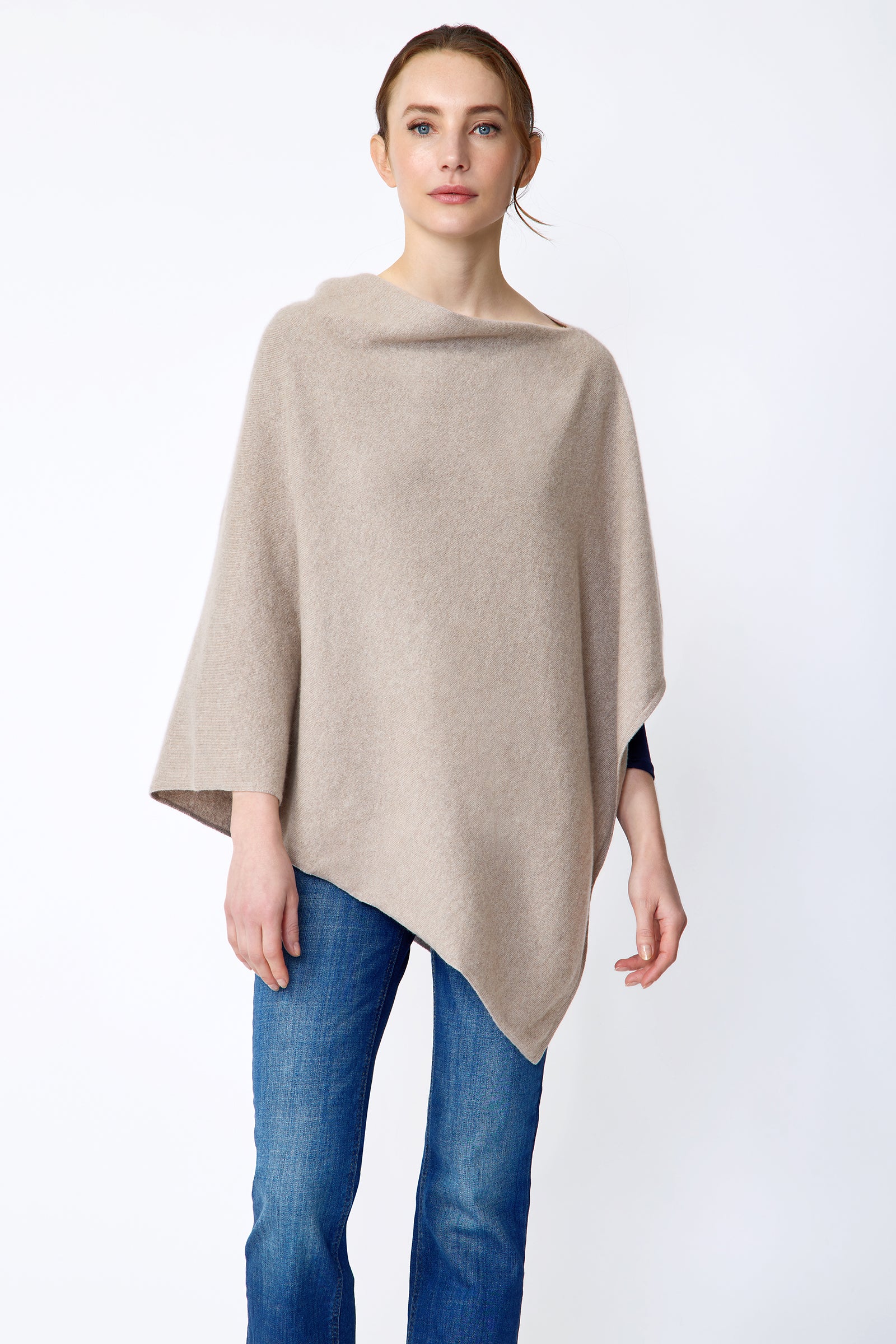 Woman wearing Kal Rieman Poncho in Drift over a blue top and blue jeans on a white background