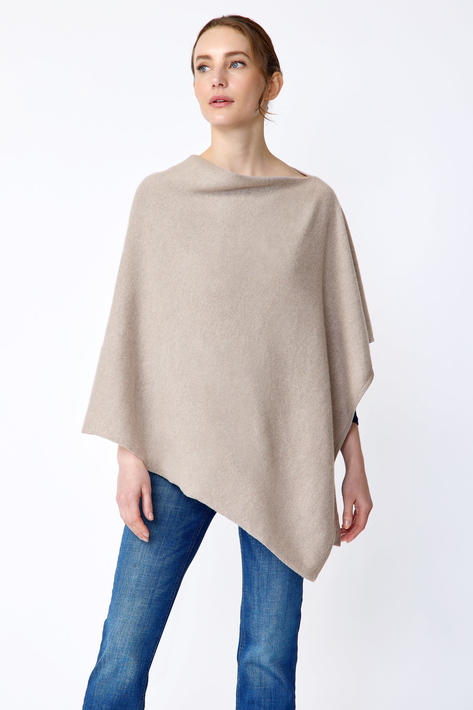 Woman wearing Kal Rieman Poncho in Drift over a blue top and blue jeans on a white background arms on the side