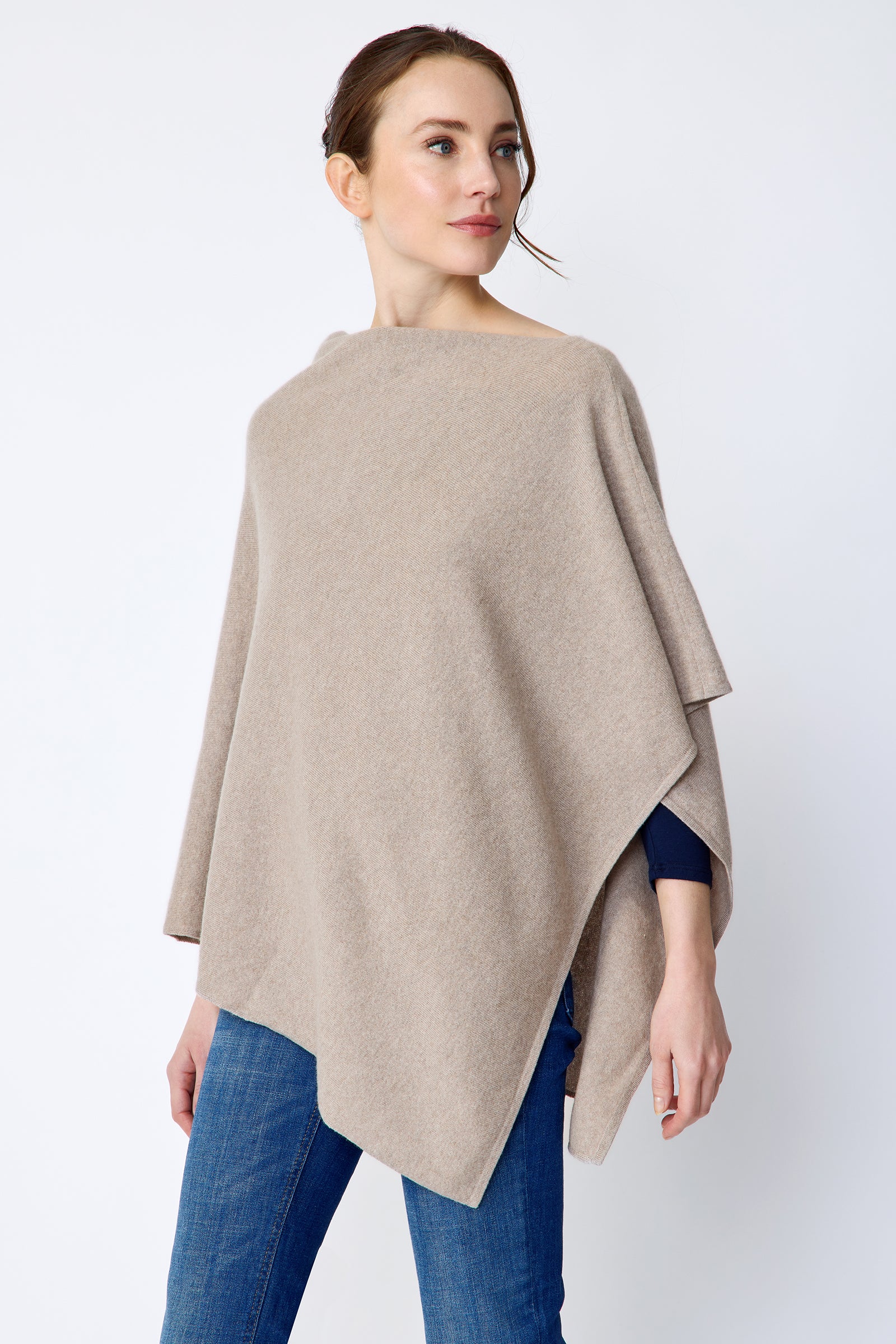 Woman wearing Kal Rieman Poncho in Drift over a blue top and blue jeans on a white background side view arms in movement