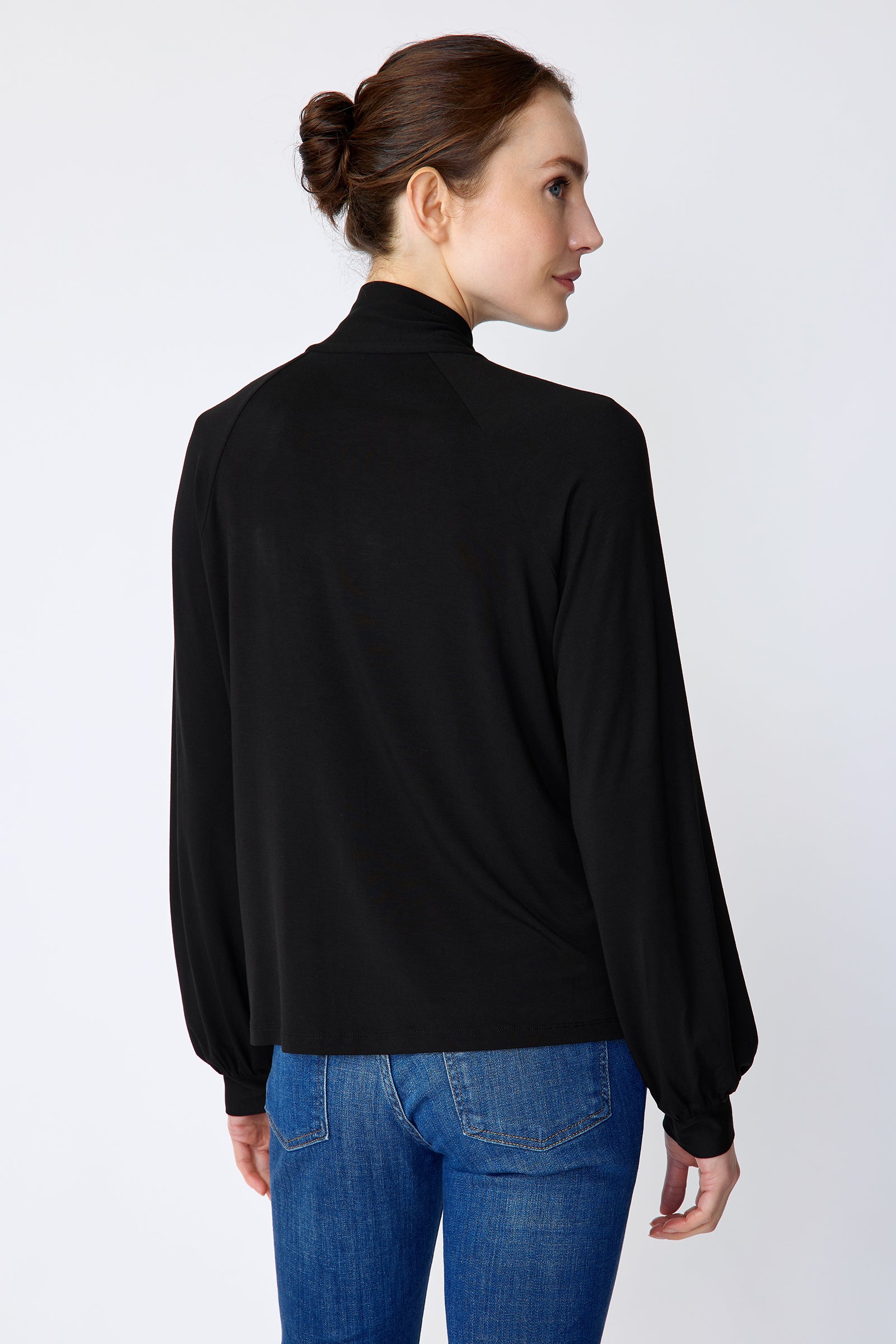 Woman wearing Kal Rieman Cecilia Scarf Top in Black and blue jeans on a white background, arm on the side, hand in pant pocket, close view