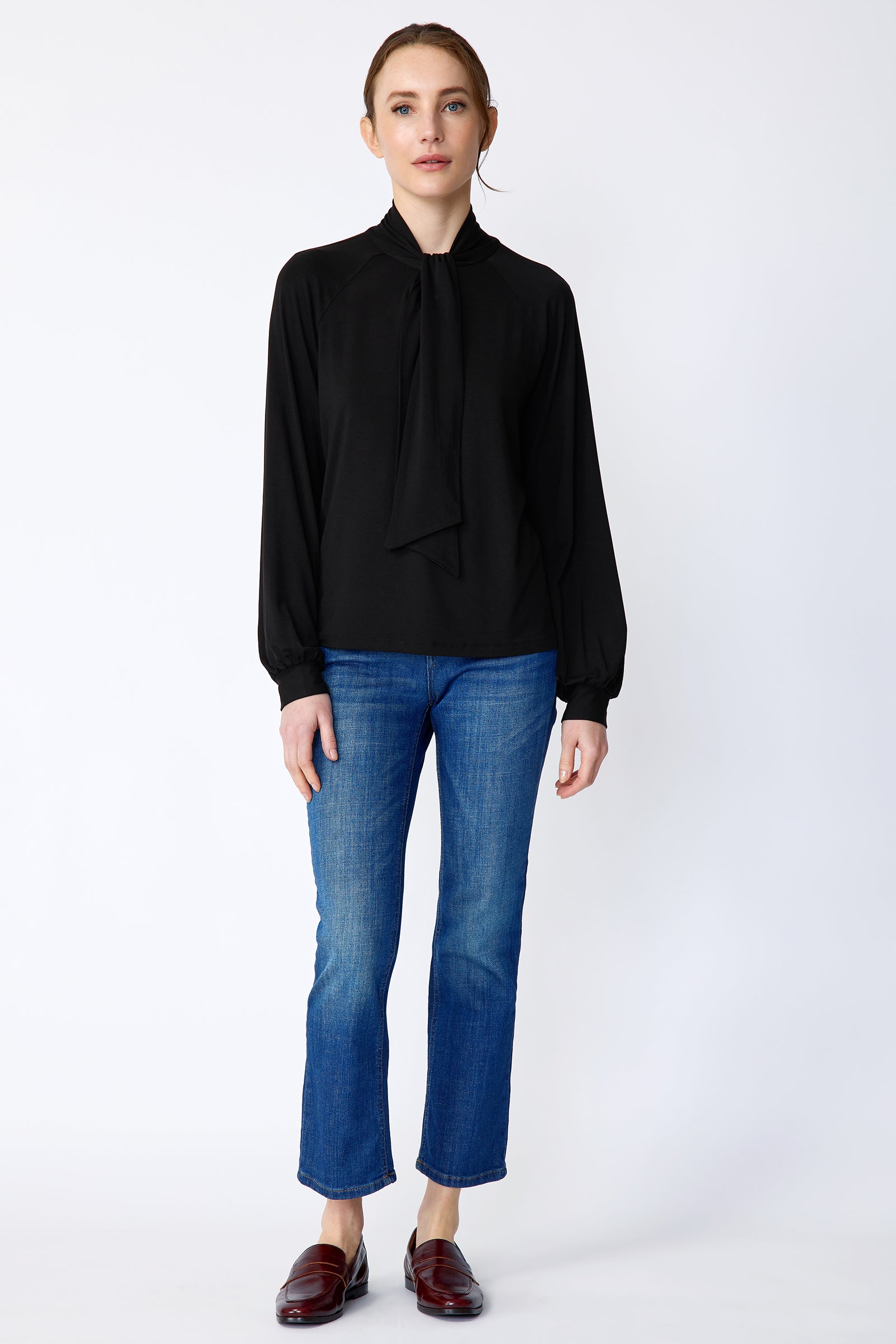 Woman wearing Kal Rieman Cecilia Scarf Top in Black and blue jeans on a white background, arms on the side