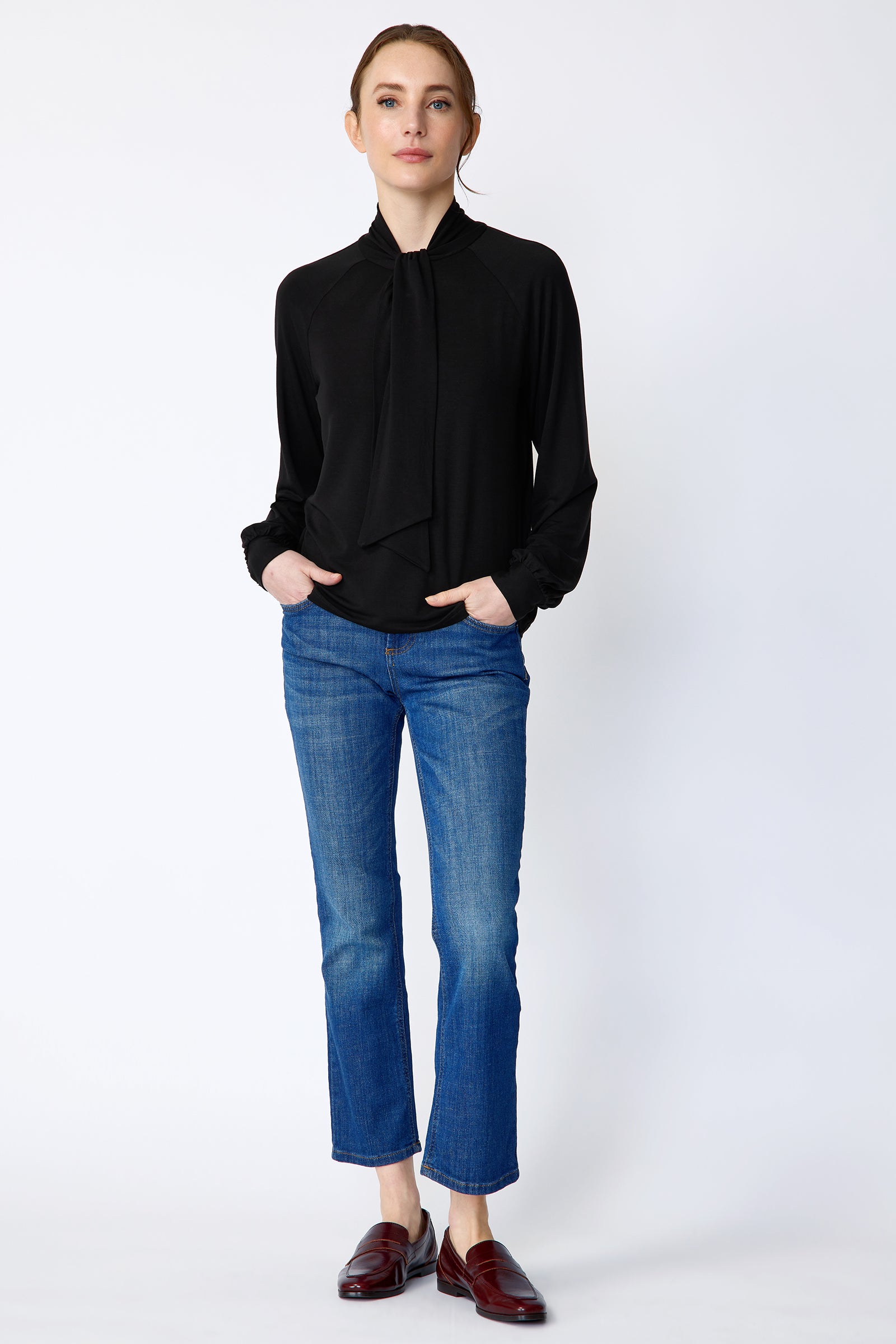 Woman wearing Kal Rieman Cecilia Scarf Top in Black and blue jeans on a white background, hands in pockets