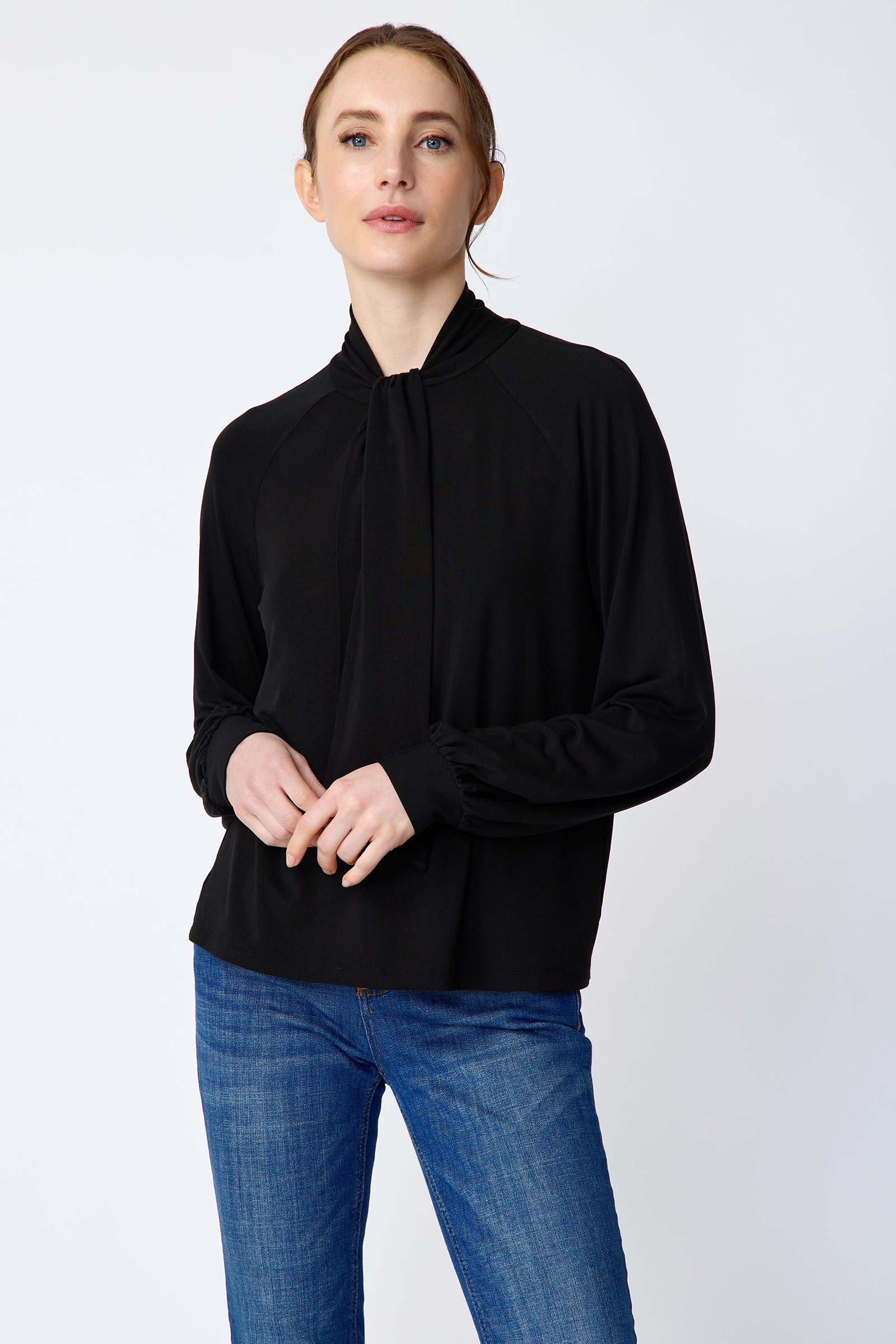 Woman wearing Kal Rieman Cecilia Scarf Top in Black and blue jeans on a white background, holding hands in front, close view