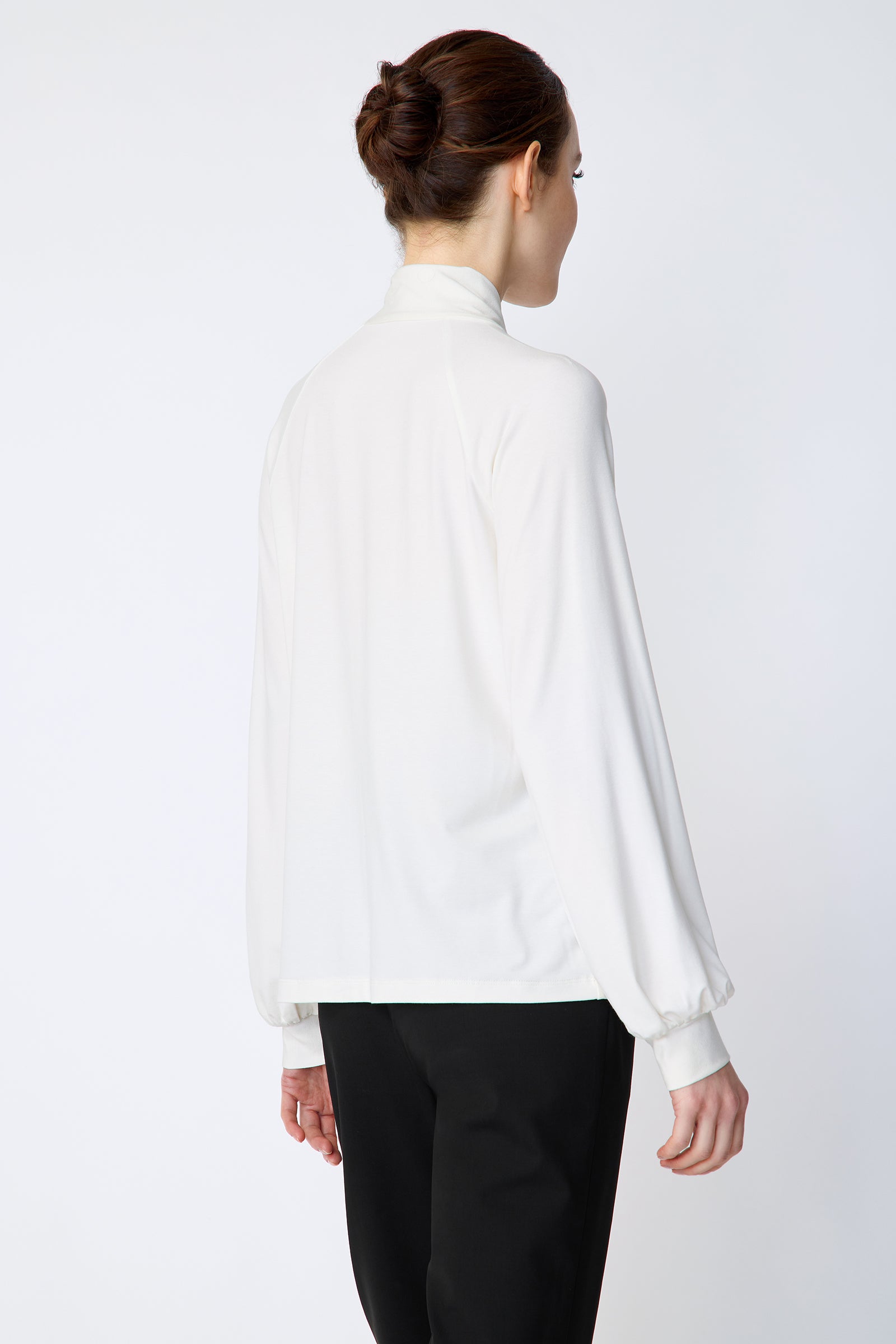 Woman wearing Kal Rieman Cecilia Scarf Top in Ivory and black pants on a white background, hands in pant pockets, close view
