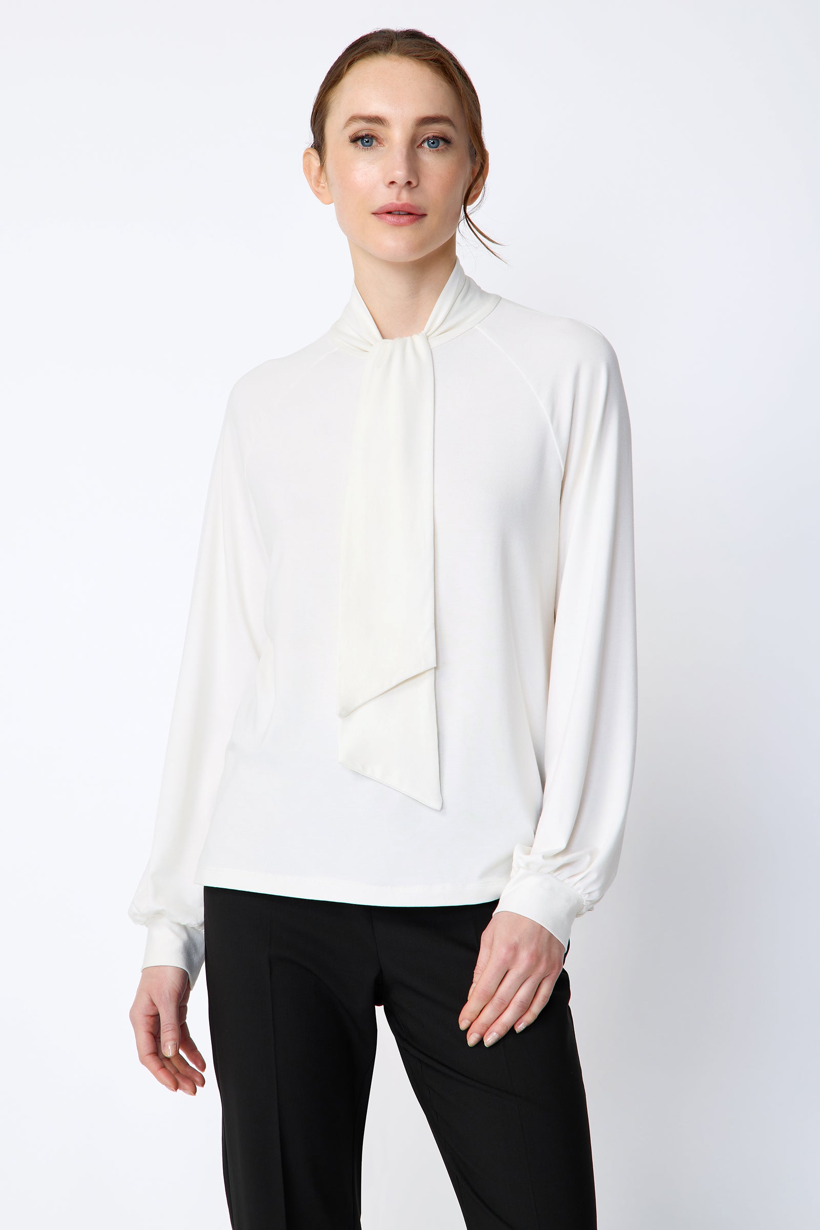 Woman wearing Kal Rieman Cecilia Scarf Top in Ivory and black pants on a white background, arms in movement