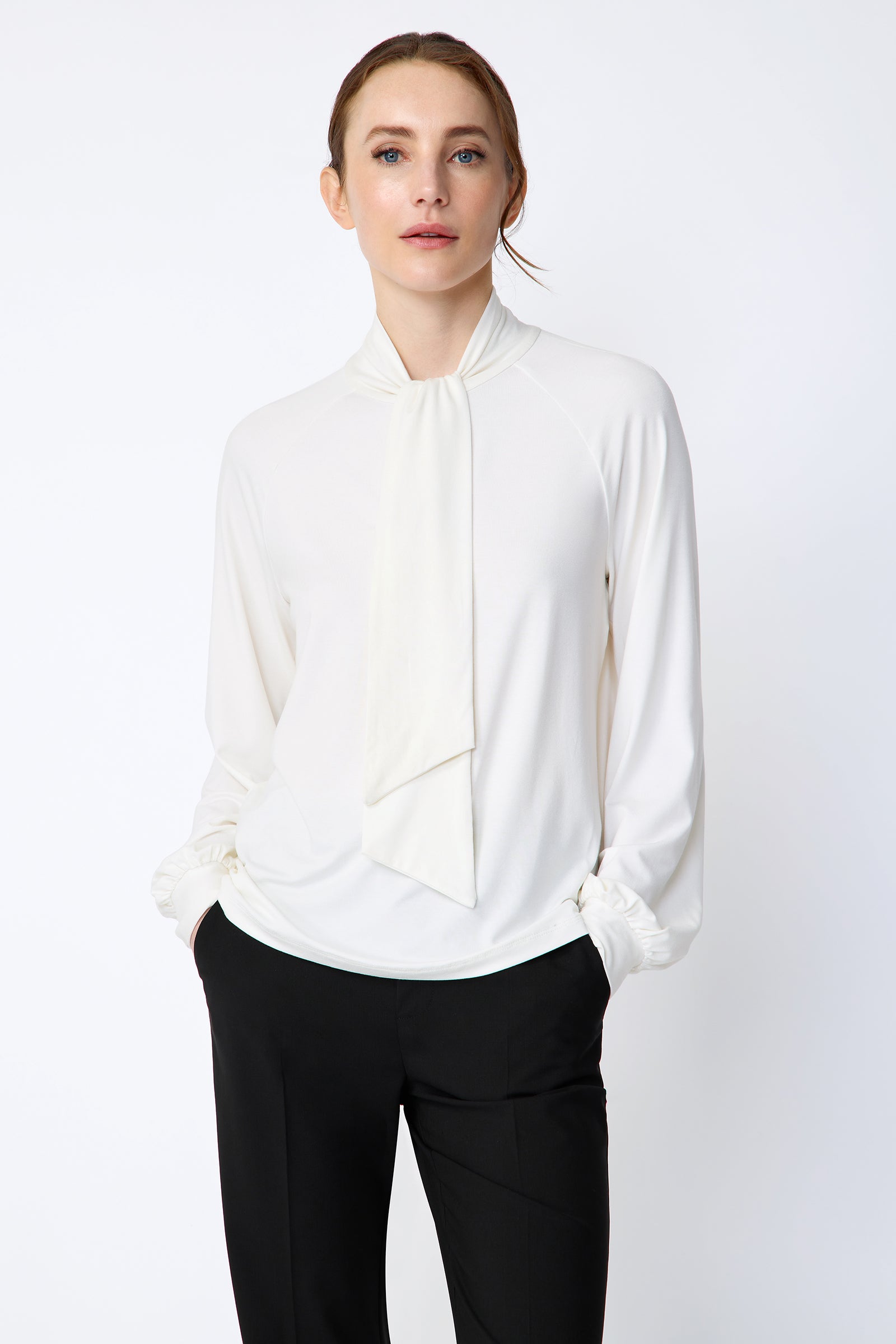 Woman wearing Kal Rieman Cecilia Scarf Top in Ivory and black pants on a white background, hands in pant pockets, close view
