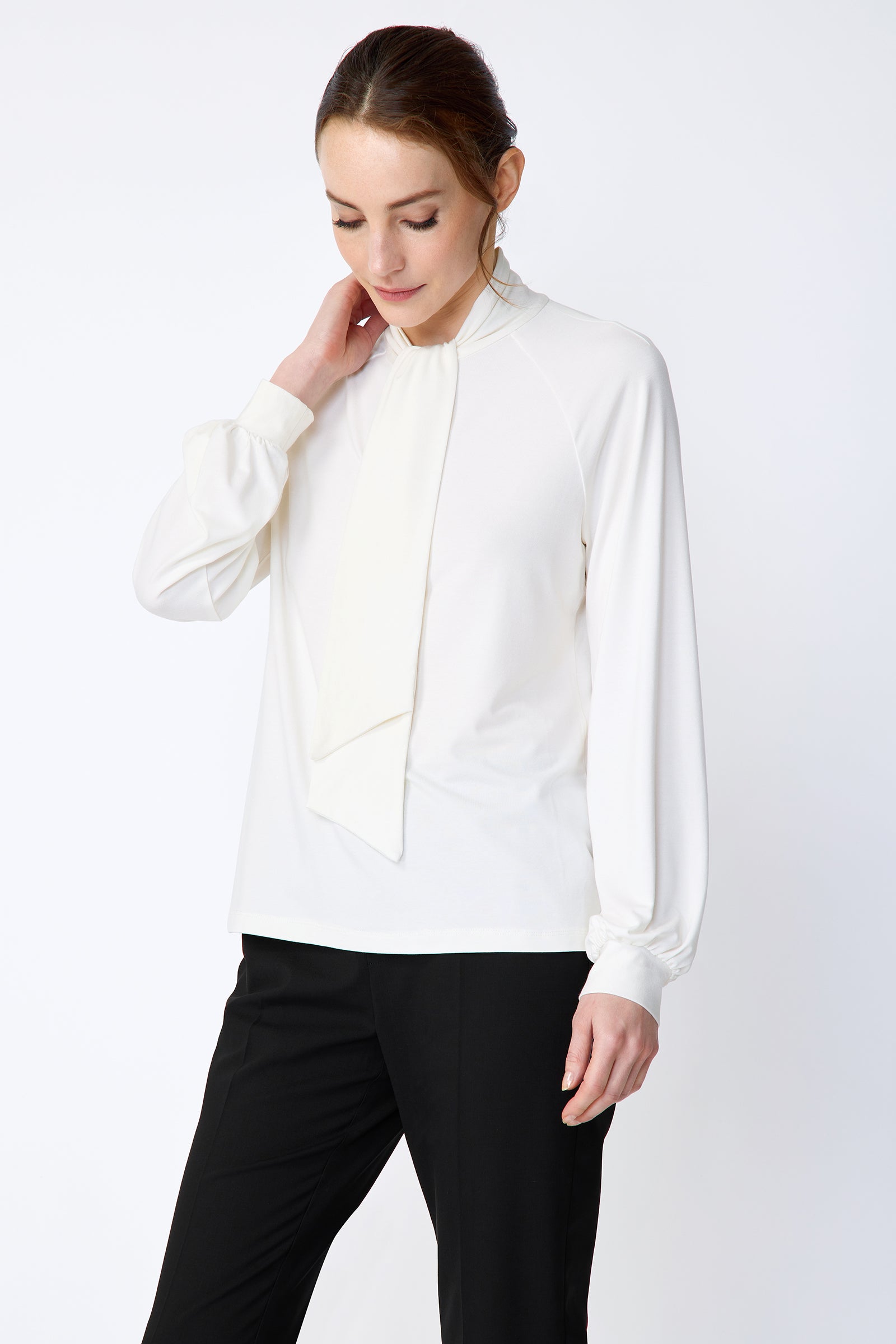 Woman wearing Kal Rieman Cecilia Scarf Top in Ivory and black pants on a white background, holding collar and arm on the side looking down, close view