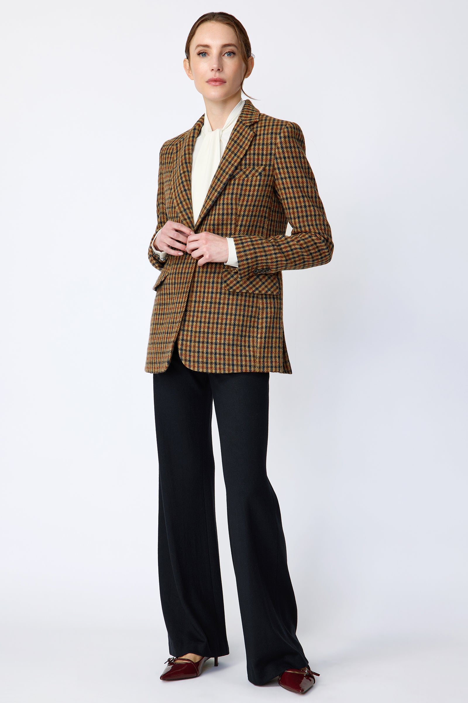 Woman wearing Kal Rieman Classic Tailored Blazer in Heritage Check over Kal Rieman Cecilia Scarf Top in Ivory with black pants, holding arms on the front