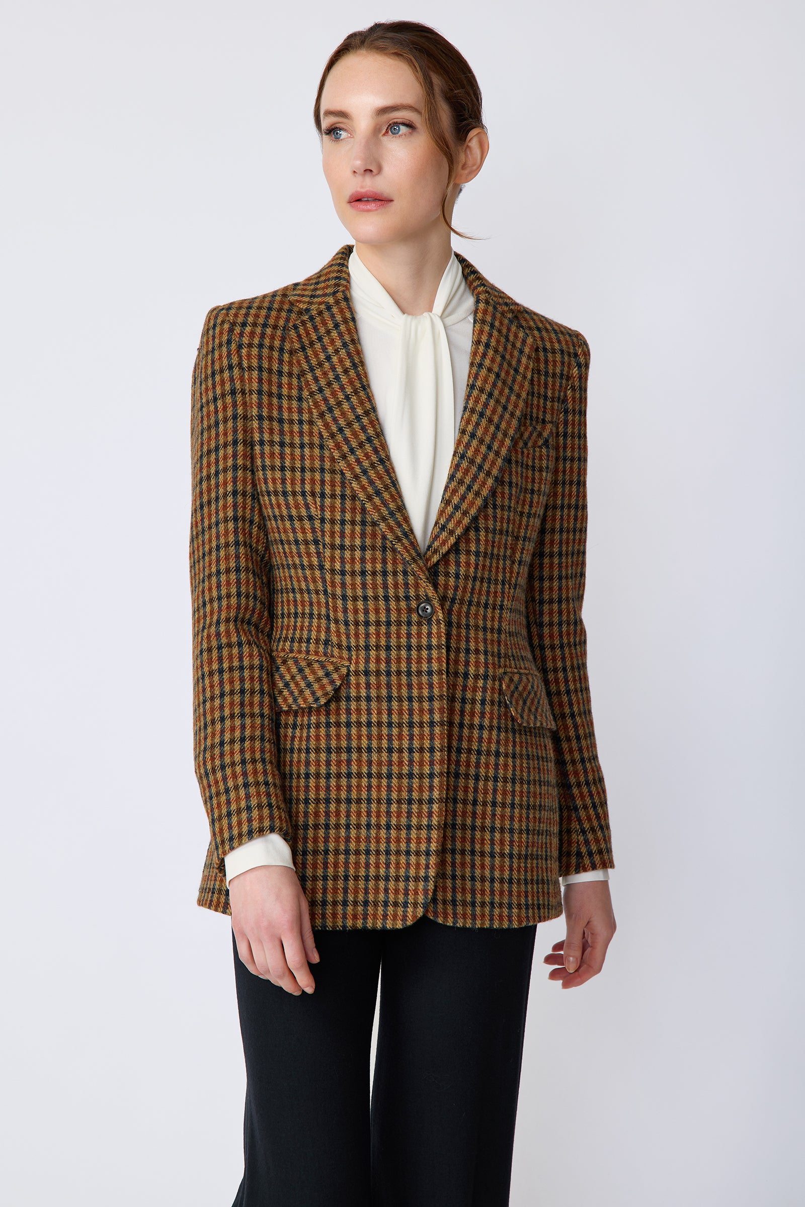 Woman wearing Kal Rieman Classic Tailored Blazer in Heritage Check over Kal Rieman Cecilia Scarf Top in Ivory with black pants, arms on the side, looking sideways