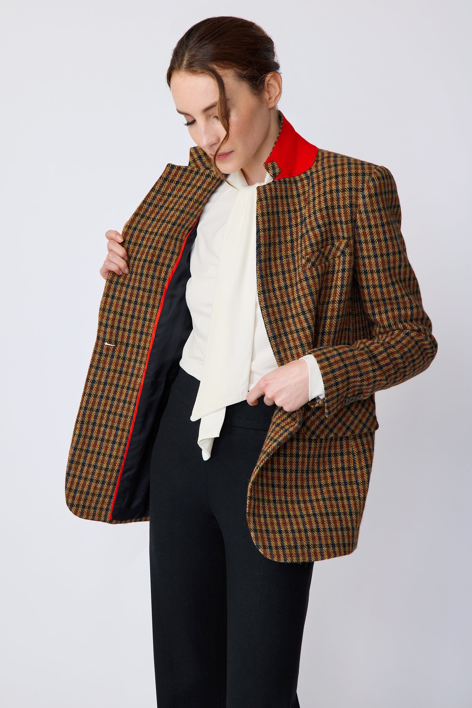 Woman wearing Kal Rieman Classic Tailored Blazer in Heritage Check over Kal Rieman Cecilia Scarf Top in Ivory with black pants, holding unbuttoned blazer, looking down