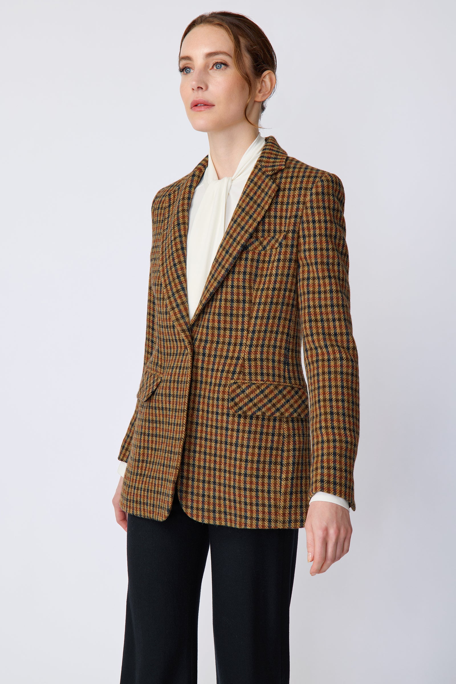 Woman wearing Kal Rieman Classic Tailored Blazer in Heritage Check over Kal Rieman Cecilia Scarf Top in Ivory with black pants, arms on the side, looking sideways