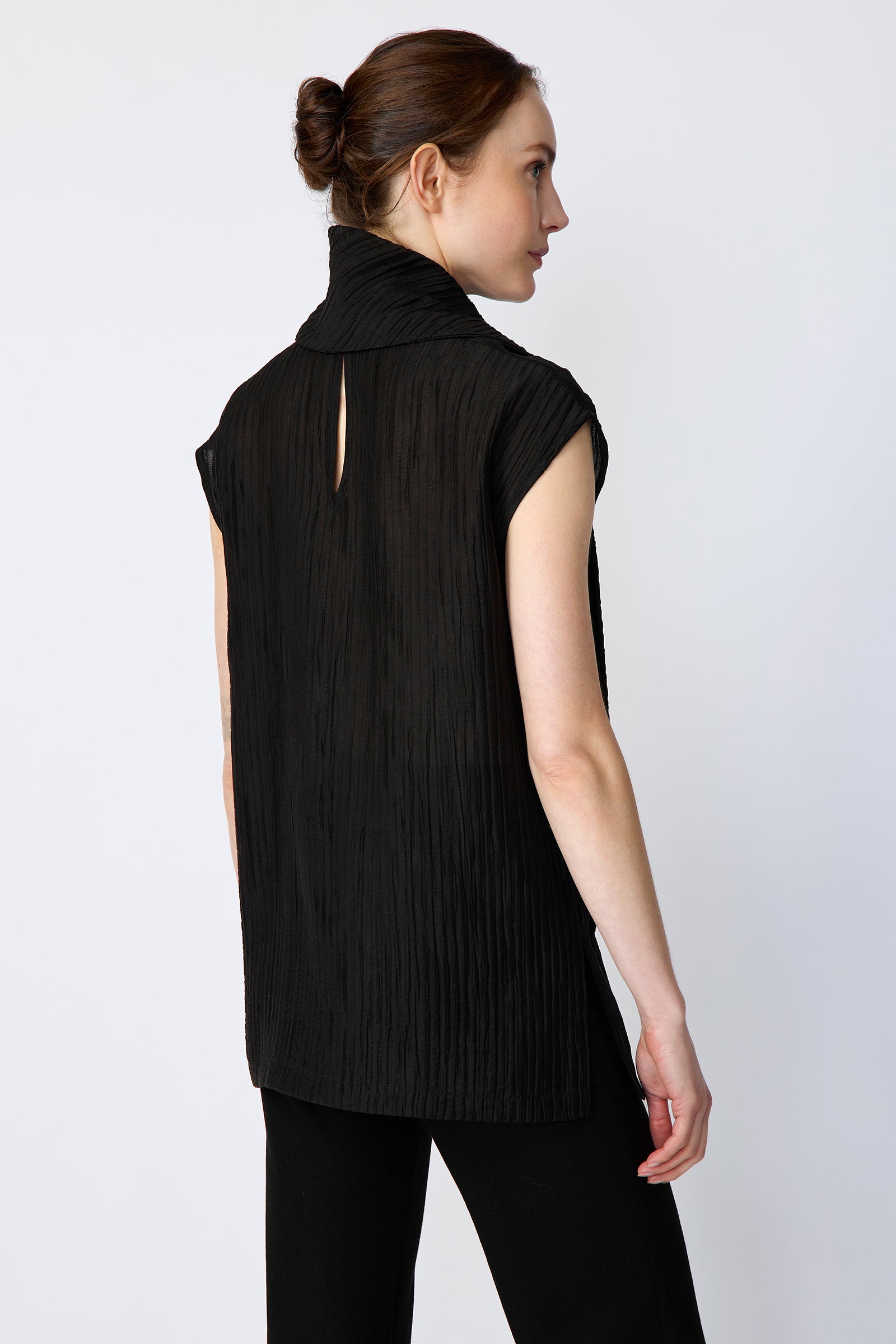 Woman wearing Kal Rieman Claudia Scarf Tunic in Black Taffeta on a white background, arms con the side, back view