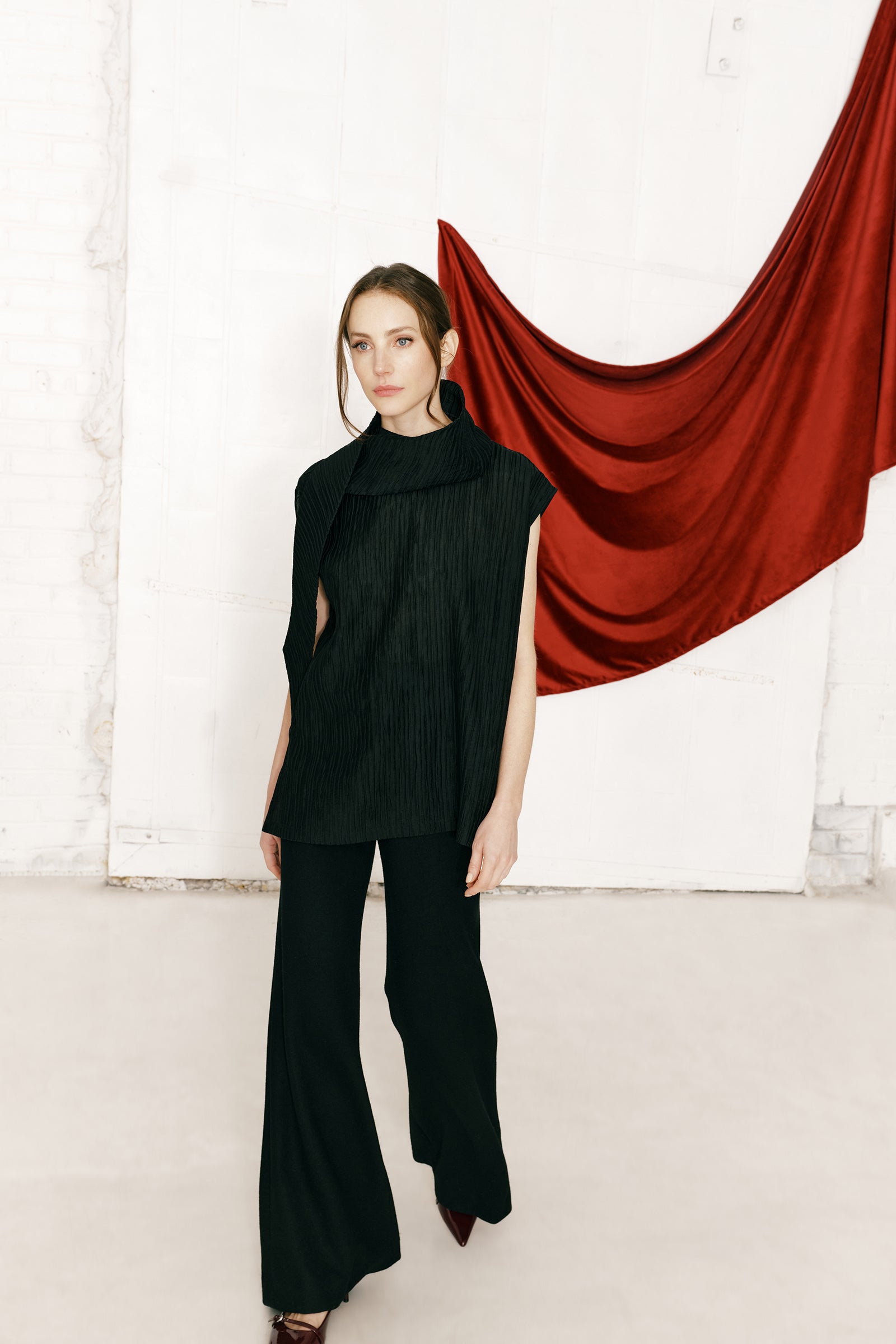 Woman wearing Kal Rieman Claudia Scarf Tunic in Black Taffeta on a white background, arms on the side, close view