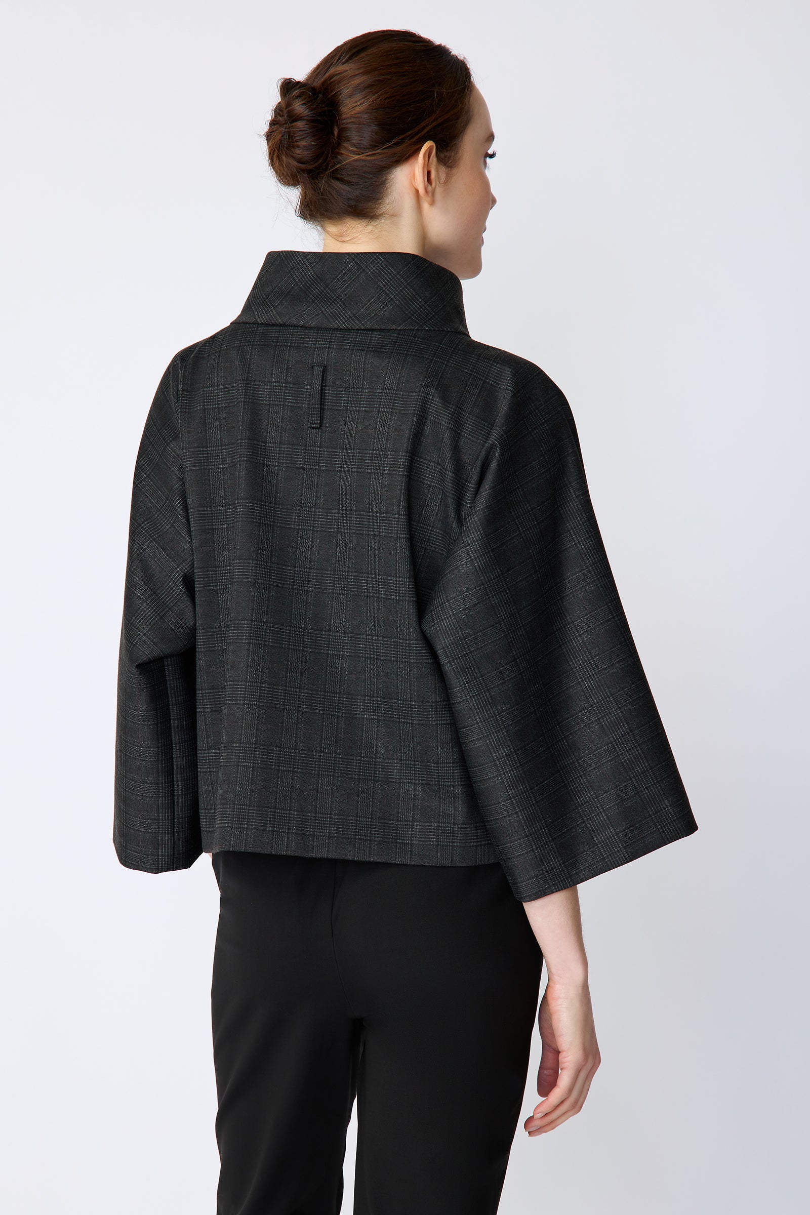 Woman wearing the Kal Rieman Edith Kimono Top in Black Glen Plaid and black pants on a white background, arm on the side back view
