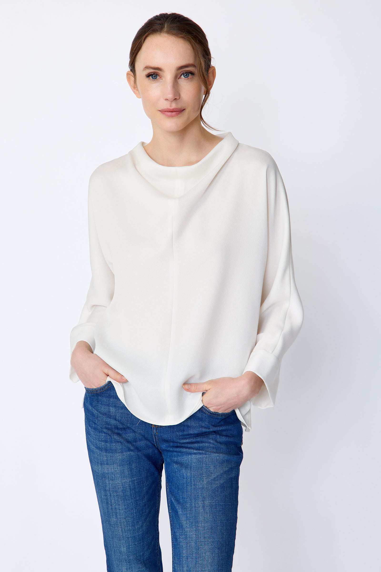 Woman wearing Kal Rieman Elena Drape Top in Ivory and blue jeans on a white background, hands in pant pockets, close view