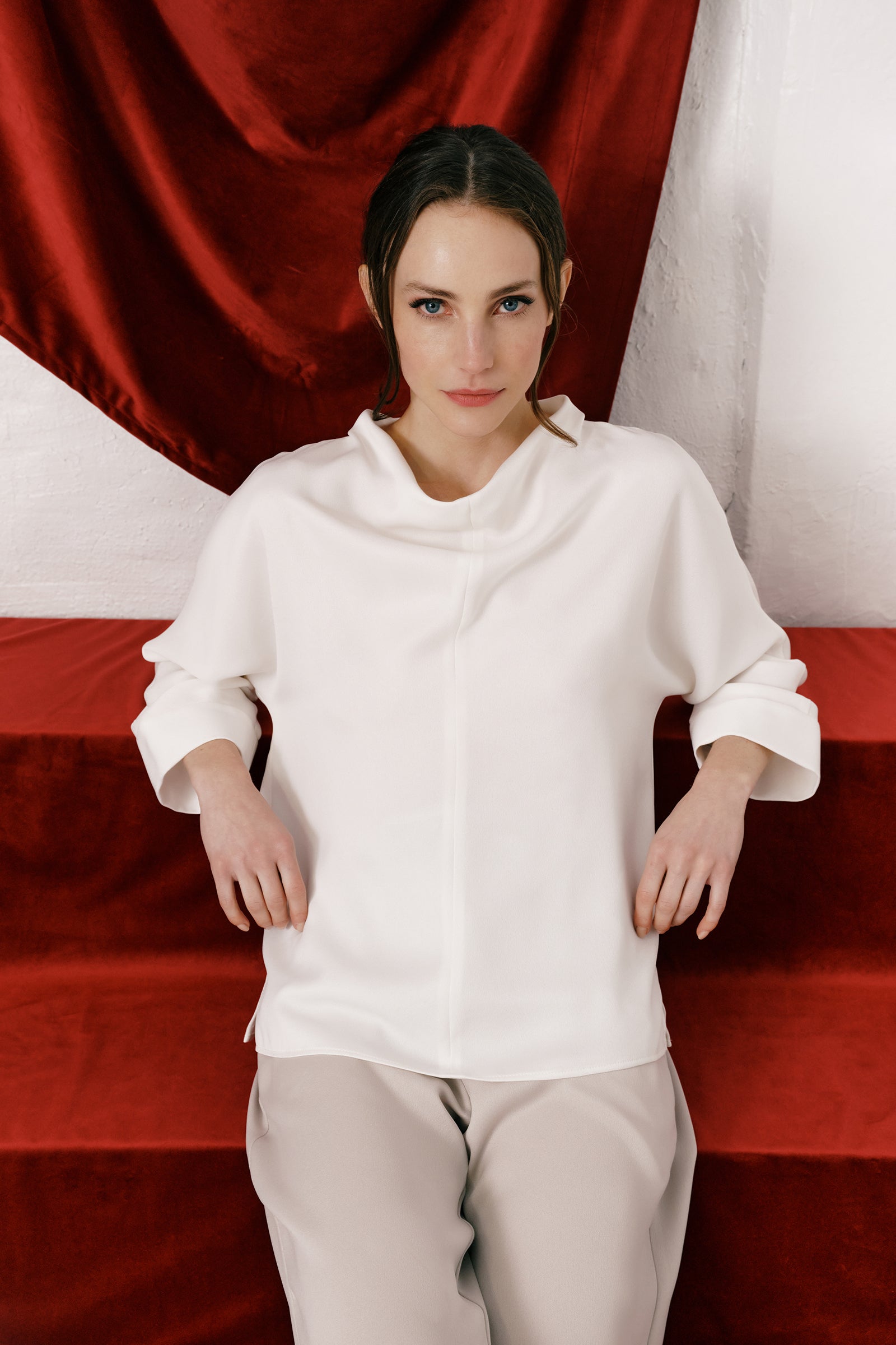 Woman wearing Kal Rieman Elena Drape Top in Ivory and blue jeans on a white background, hands in pant pockets, close view