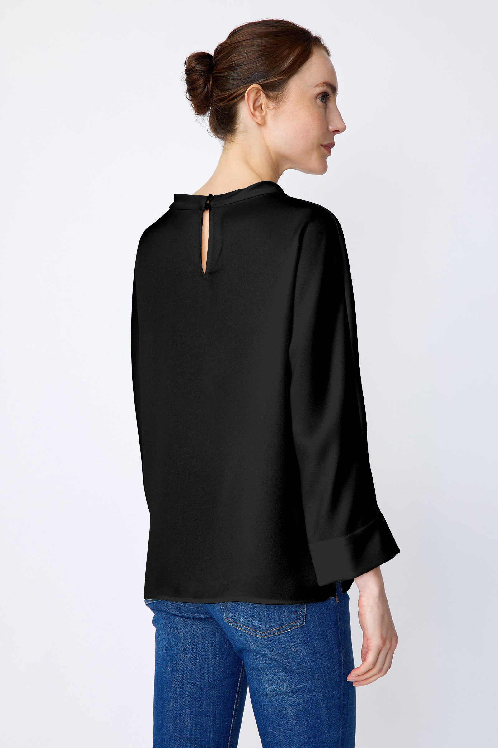 Woman wearing Kal Rieman Elena Drape Top in black satin with blue jeans, hands in pant back pockets, close front view