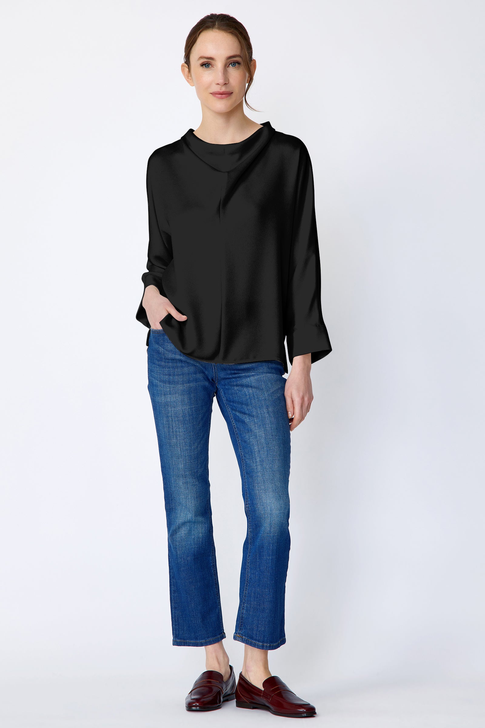 Woman wearing Kal Rieman Elena Drape Top in black satin with blue jeans, hand in pant pocket, arm on the side, full front view