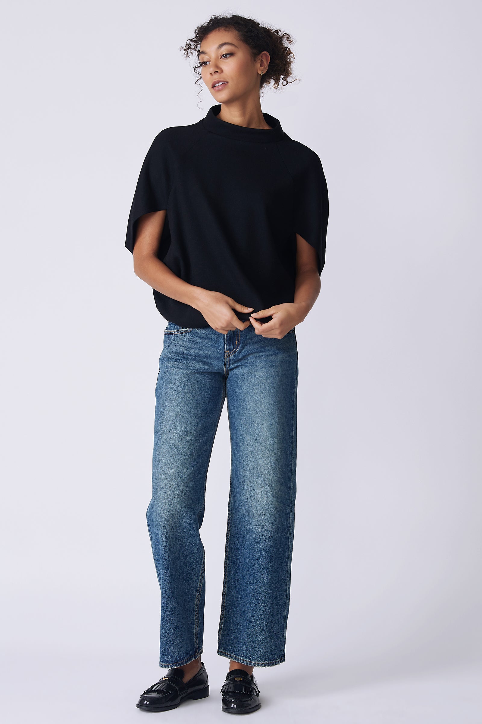 Kal Rieman Elsa Cape Top in black on model front view holding hem looking to the side