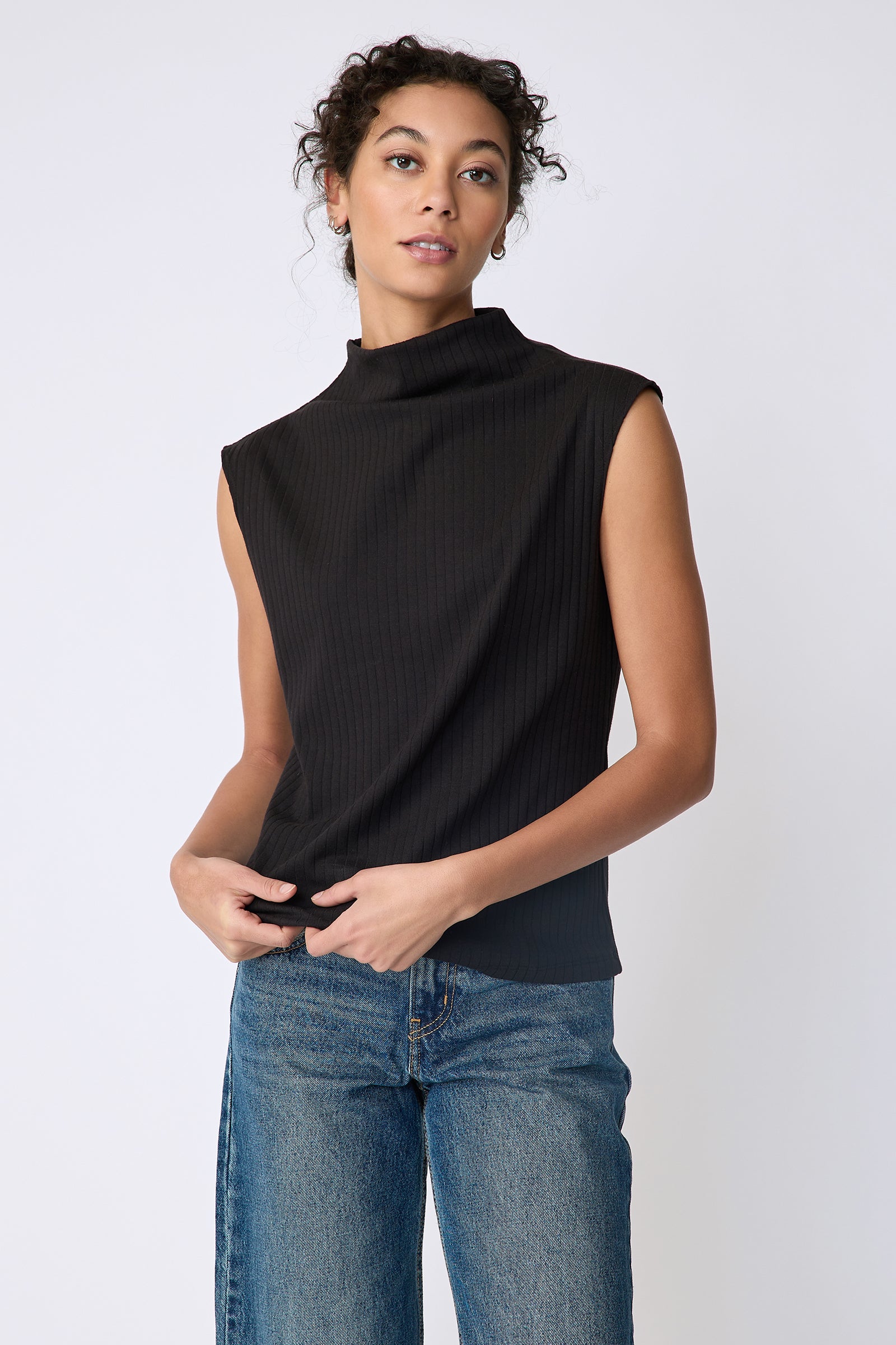 Kal Rieman Eva Funnelneck top in black rib knit on model front view holding hem