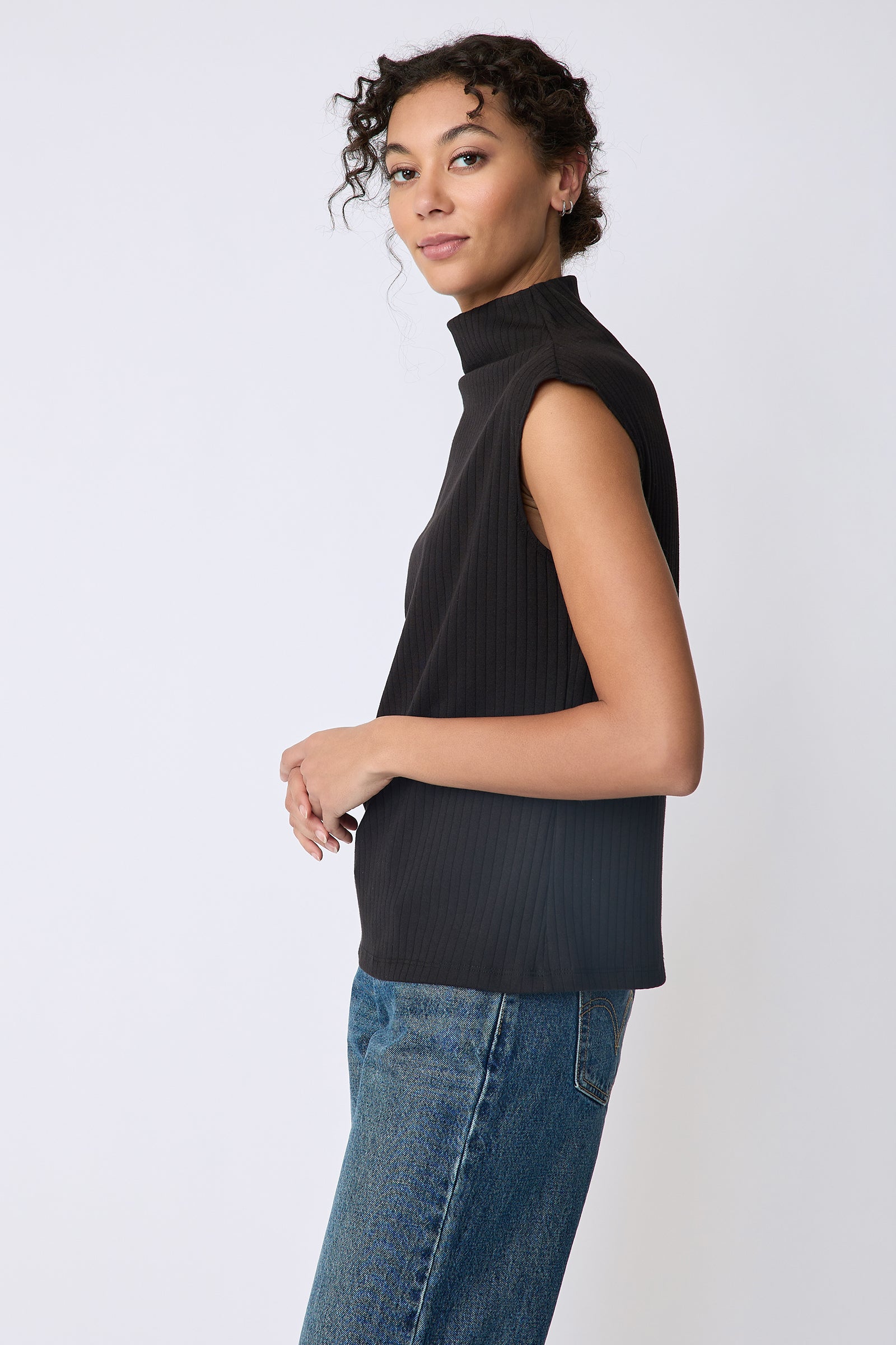Kal Rieman Eva Funnelneck top in black rib knit on model side view hands in front