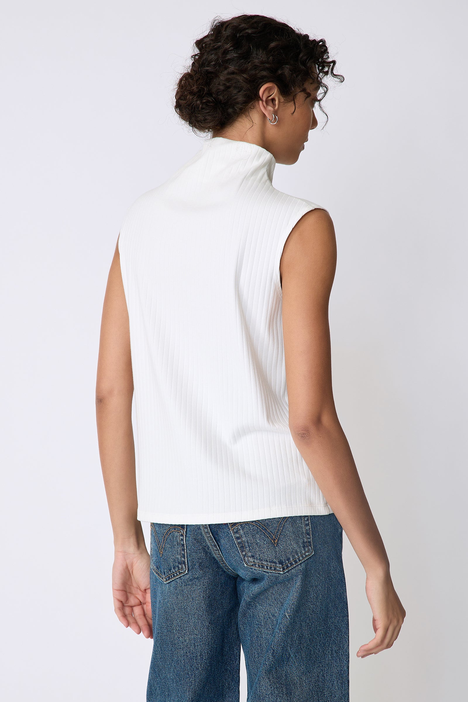 Kal Rieman Eva Funnelneck top in ivory rib knit on model front view holding hem