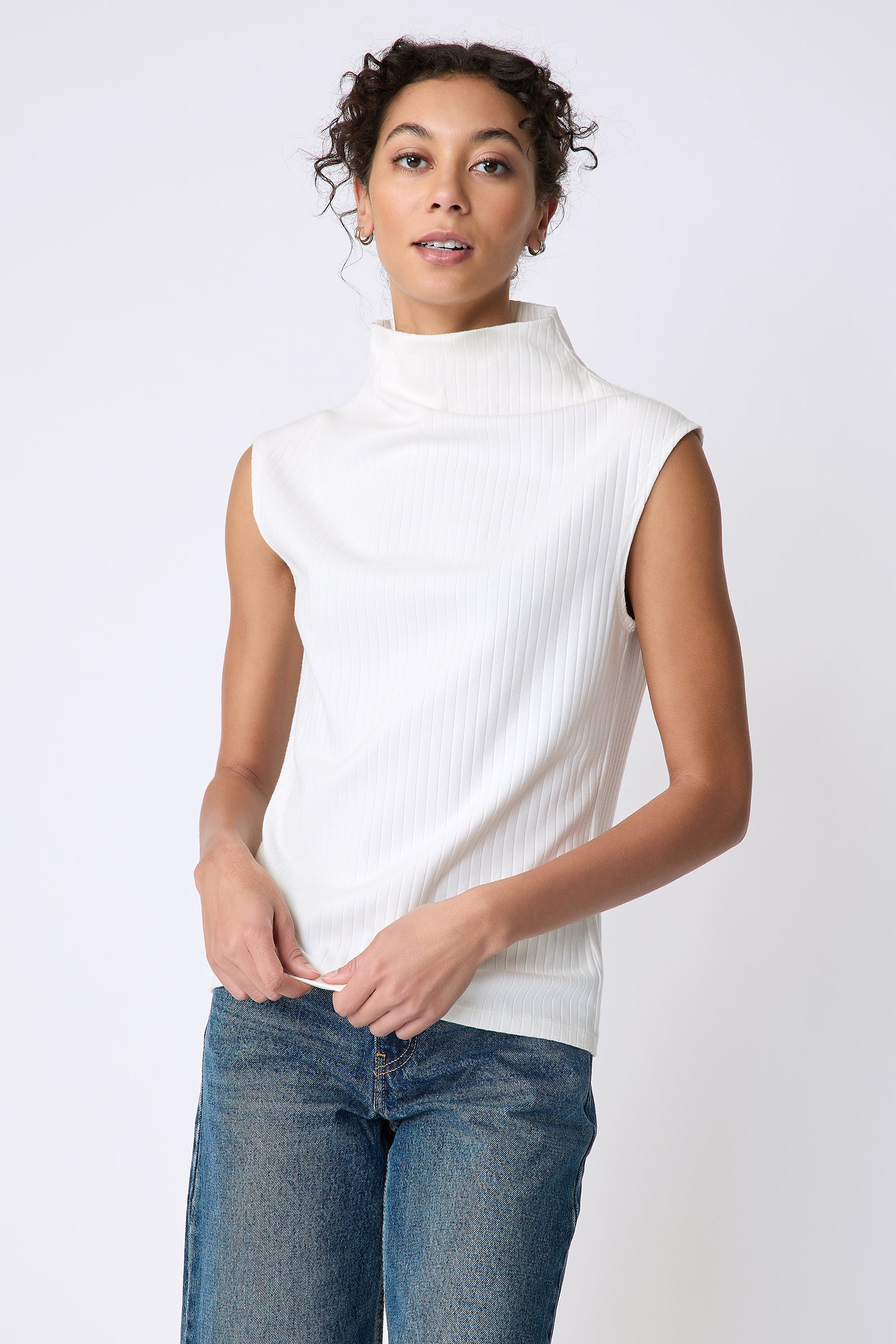 Kal Rieman Eva Funnelneck top in ivory rib knit on model front view holding hem