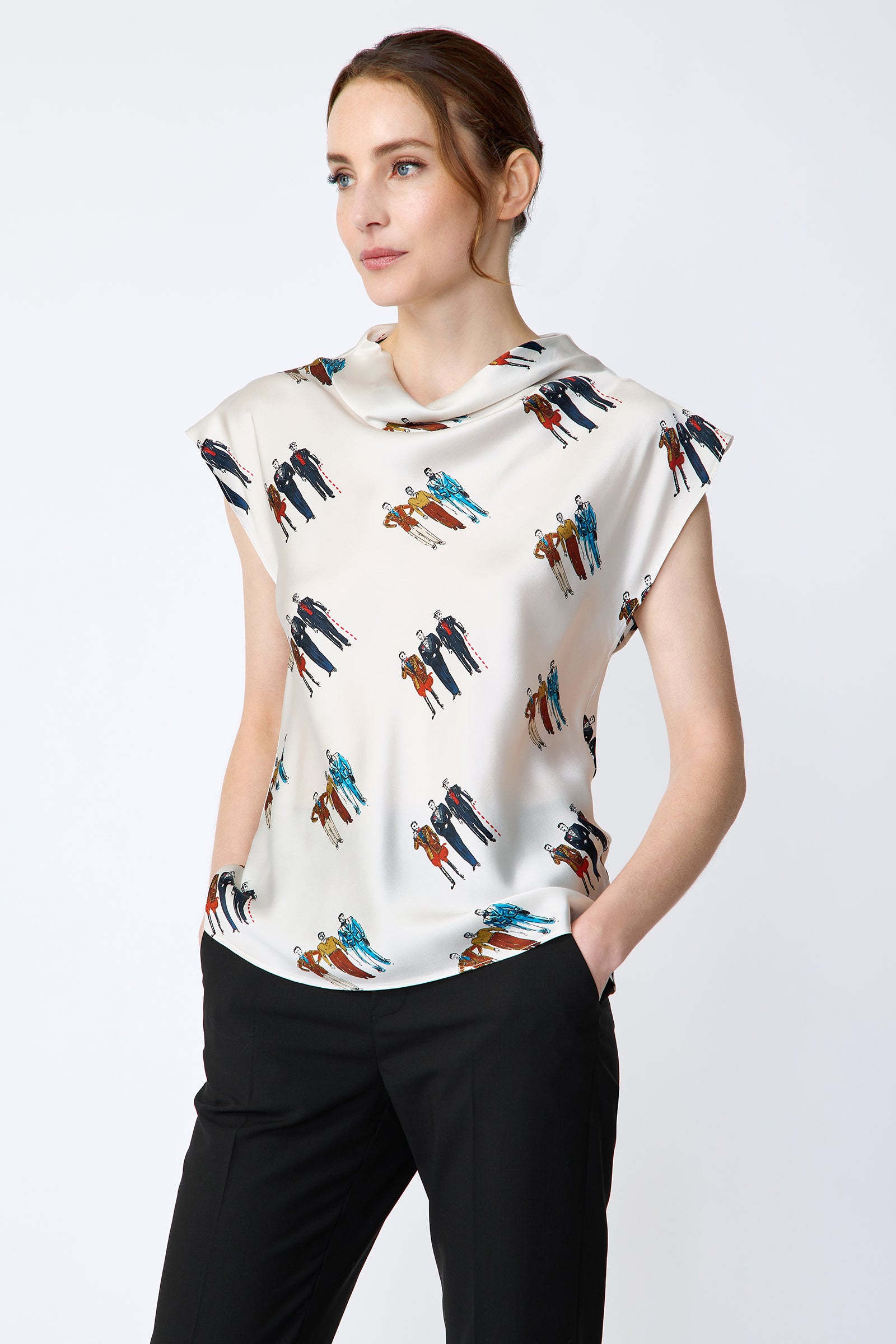 Woman wearing Kal Rieman Gloria Drape Top in Dandy Print and black pants on a white background hands in pockets, looking to the side