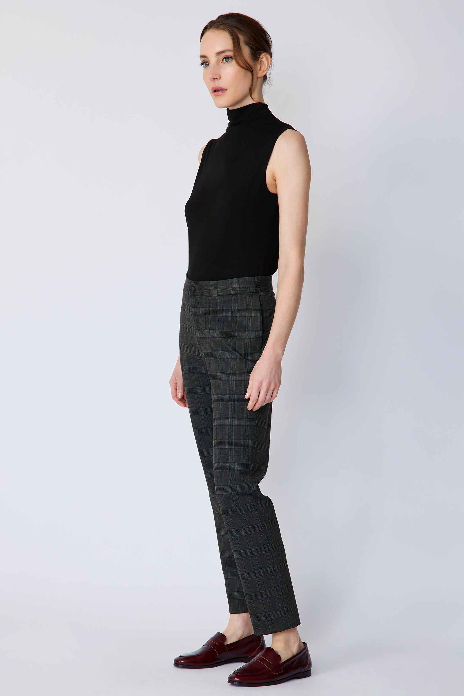 Woman wearing Kal Rieman Madison Pant in Black Glen Plaid and a black tank, arms on the side on white background, side view