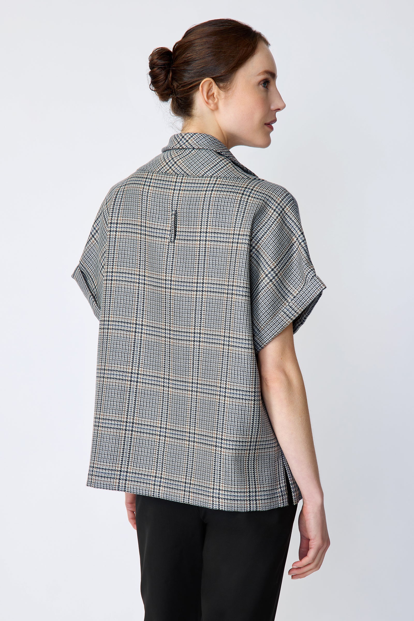 Woman wearing Kal Rieman Marin Top in Glen Plaid and black pants on a white background, arms on the side, back view