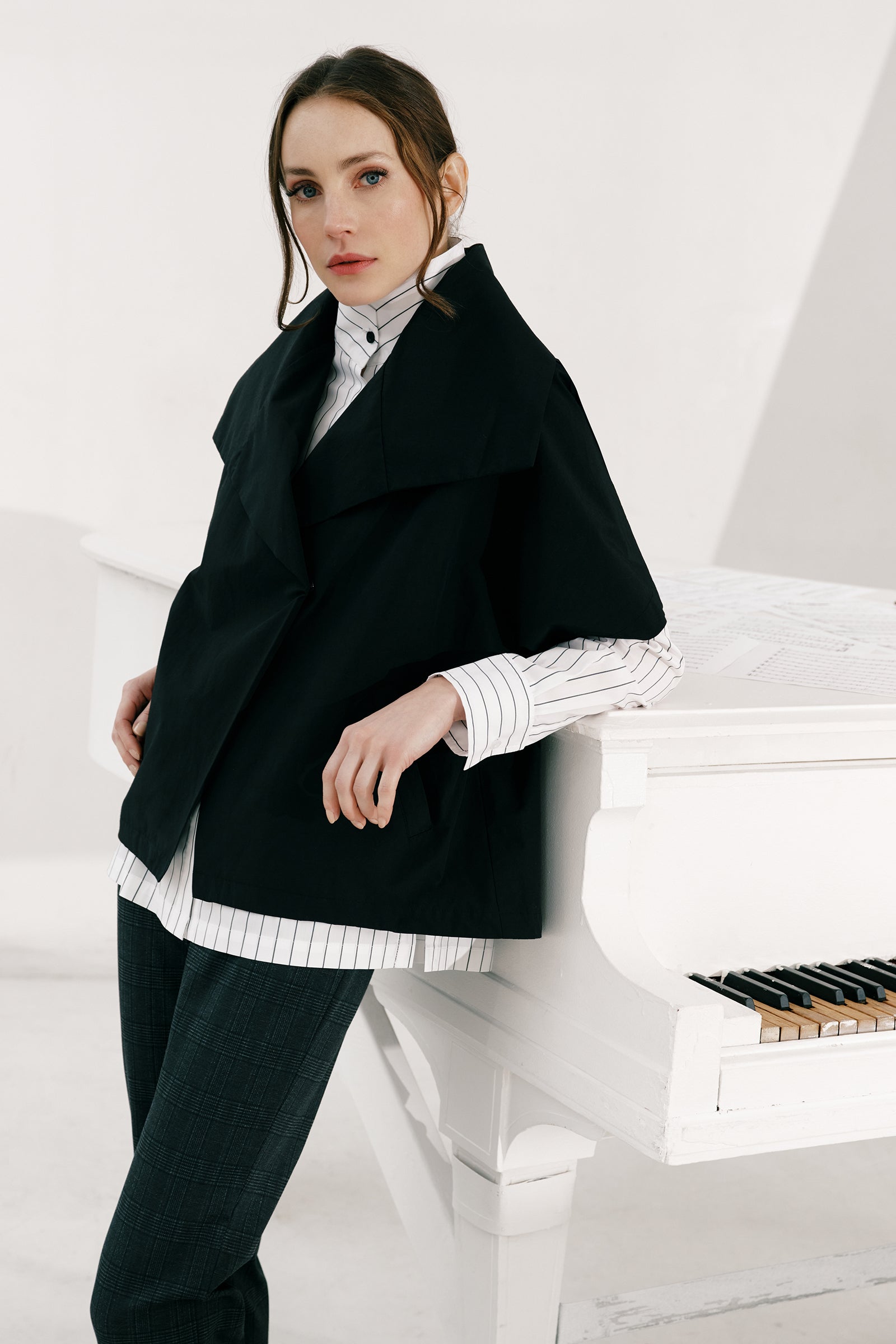 Woman wearing the Kal Rieman Paris Jacket in black over the Marlene Piano Stripe Shirt leaning on a piano look book image