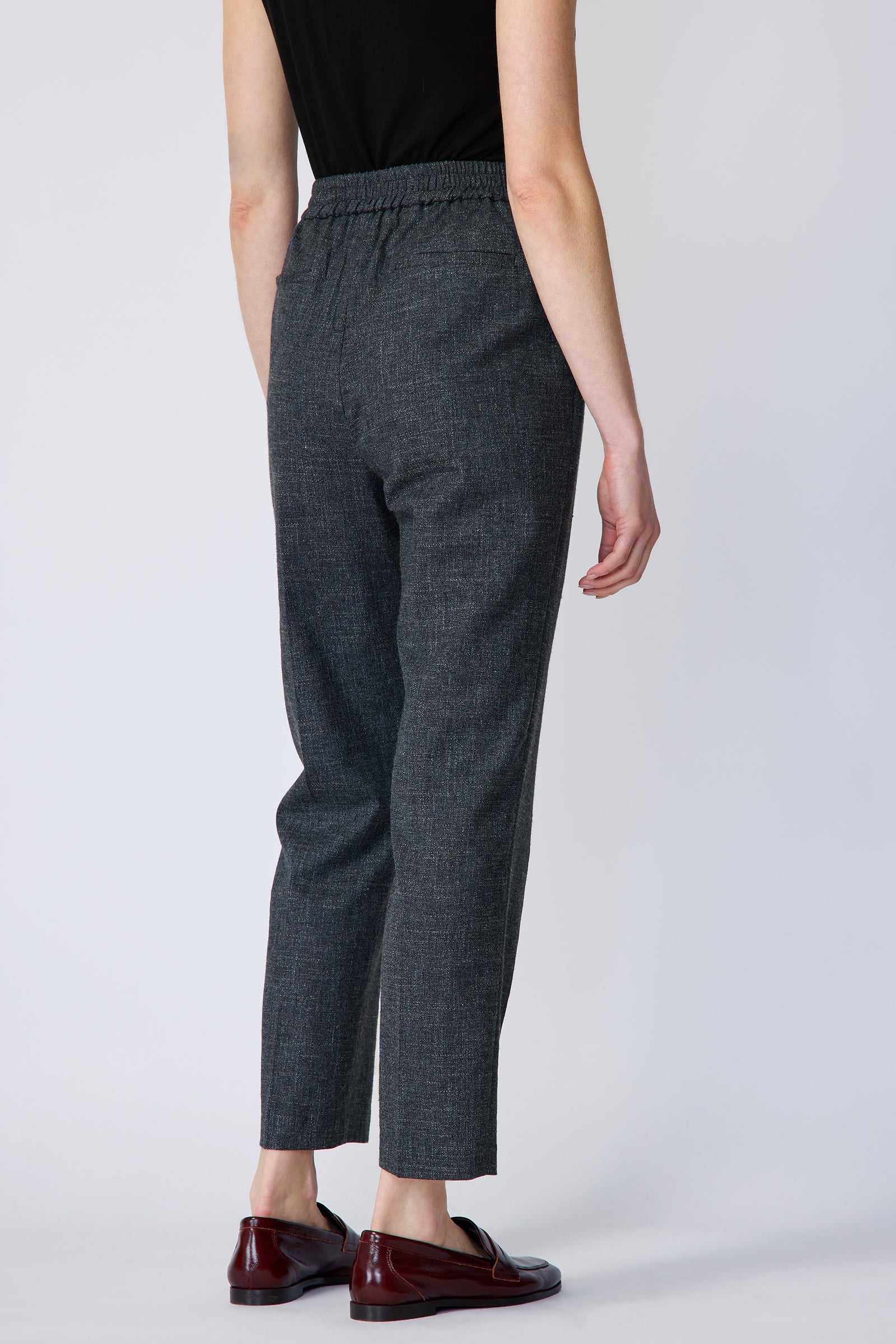 Woman wearing Kal Rieman Martine Trouser in Indigo with brown shoes, arms on the side on white background, back view