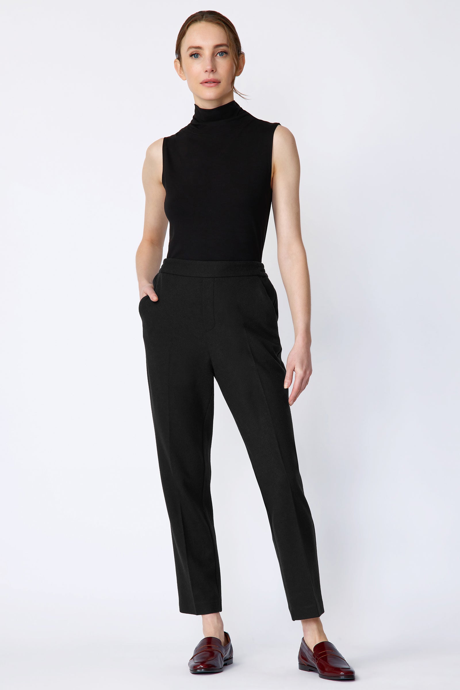 Woman wearing a black sleeveless top and black pants on a white background