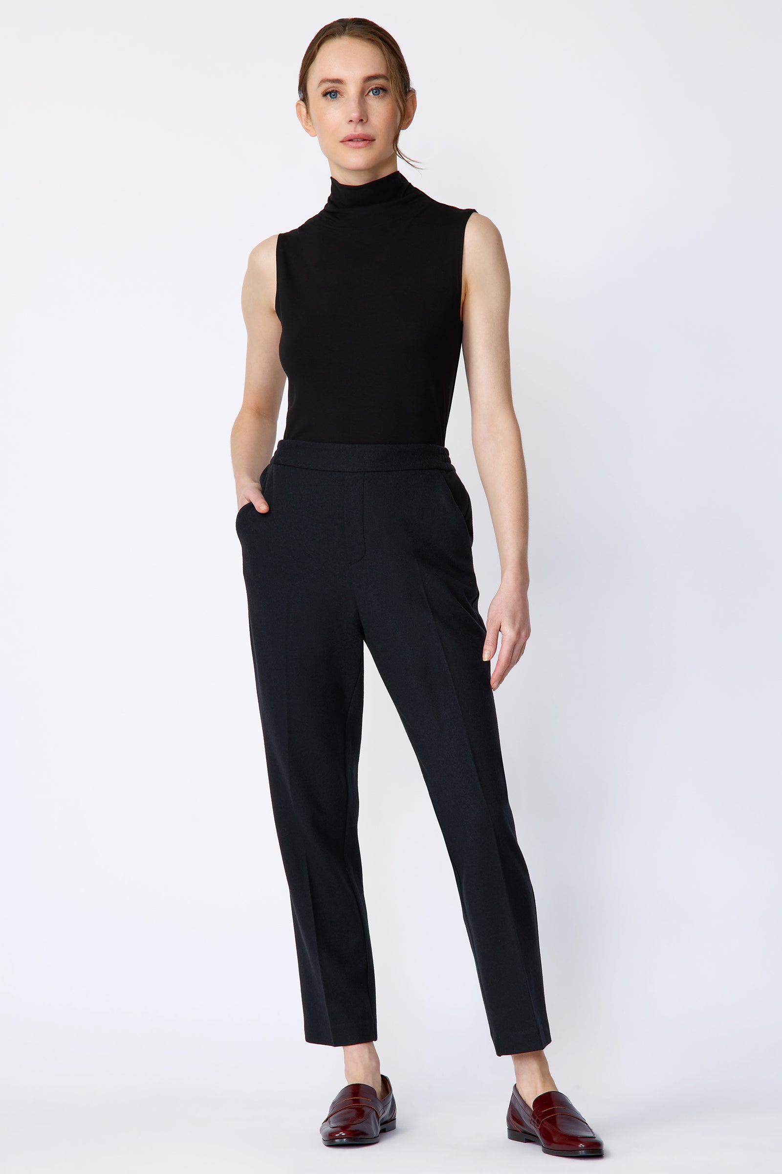 Woman wearing Kal Rieman Martine Trouser in midnight felted jersey with a black tank top and brown shoes, hand in pant pocket, arm on the side, full front view