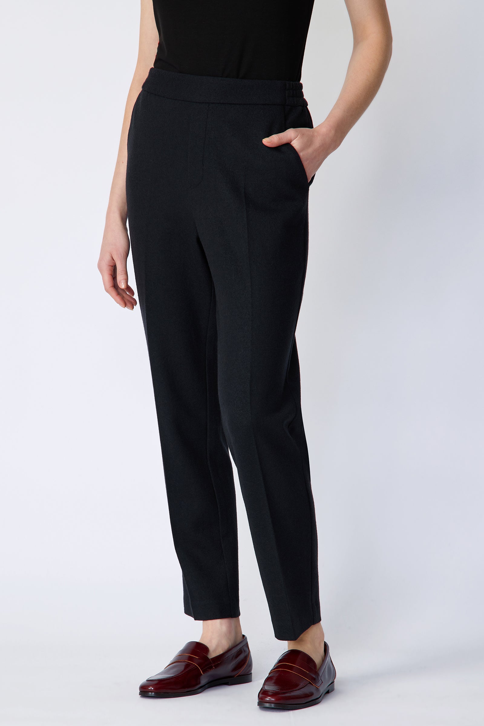 Woman wearing Kal Rieman Martine Trouser in midnight felted jersey with a black tank top and brown shoes, hand in pant pocket, arm on the side, close front view
